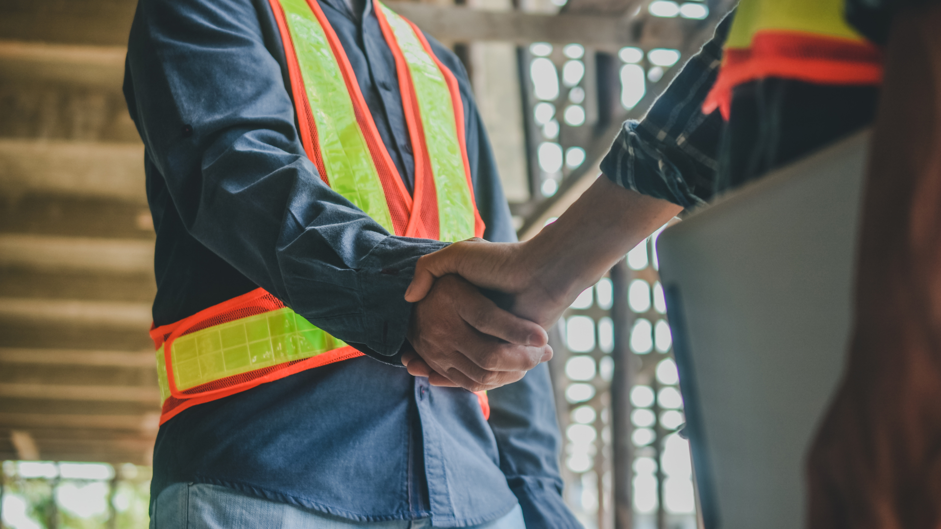 Two construction workers are shaking hands on a construction site.