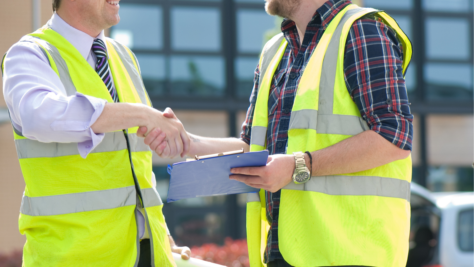 Two men in yellow vests are shaking hands while holding a clipboard.