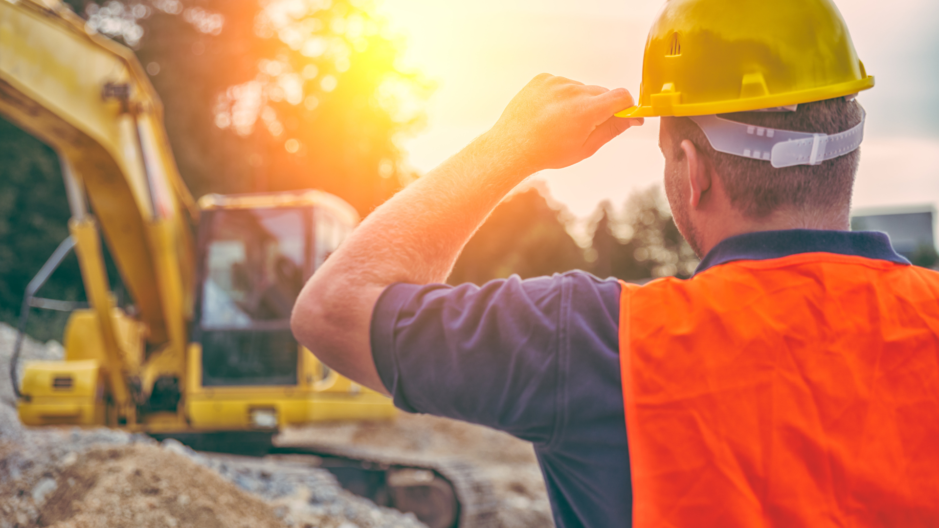 A construction worker wearing a hard hat is looking at a bulldozer on a construction site.