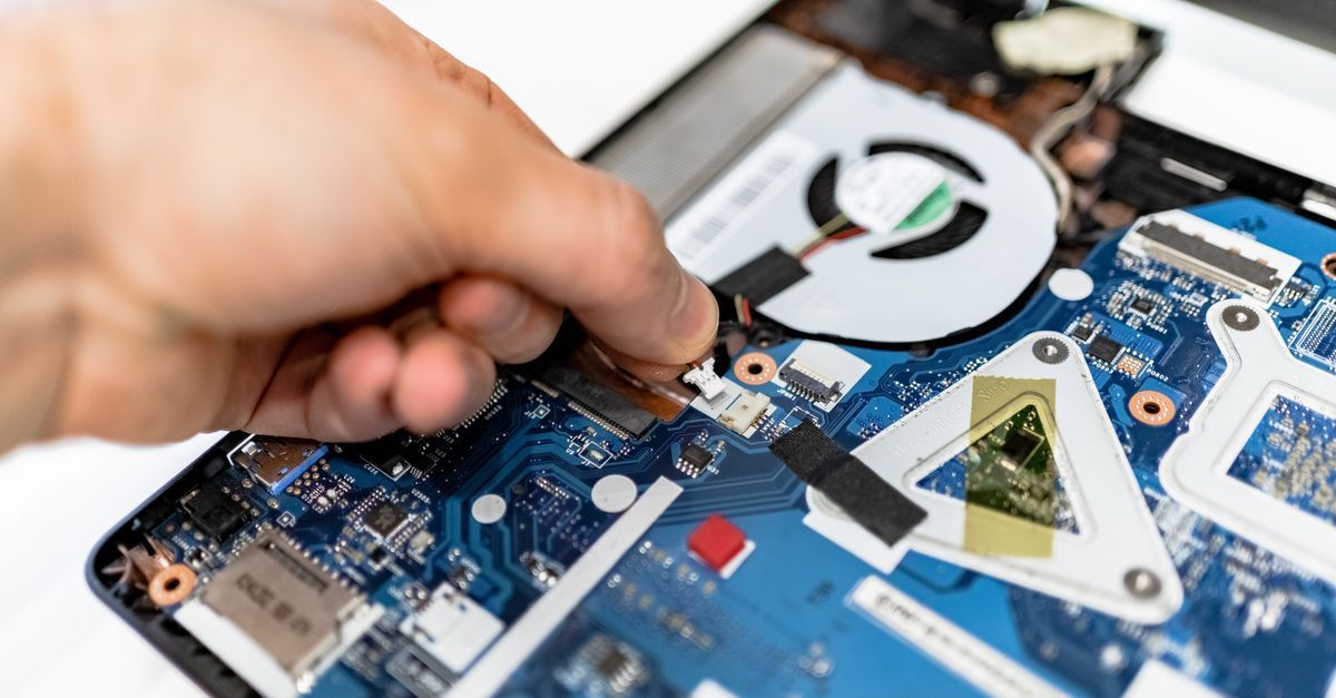 Reparación manual de la placa base de un portátil azul con un destornillador cerca del ventilador de refrigeración.