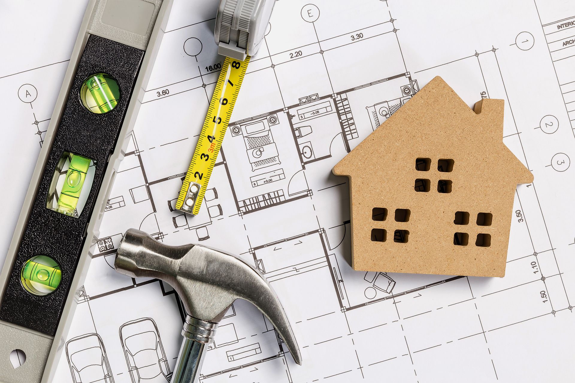 Blueprint with tools: level, tape measure, hammer, and small wooden house.