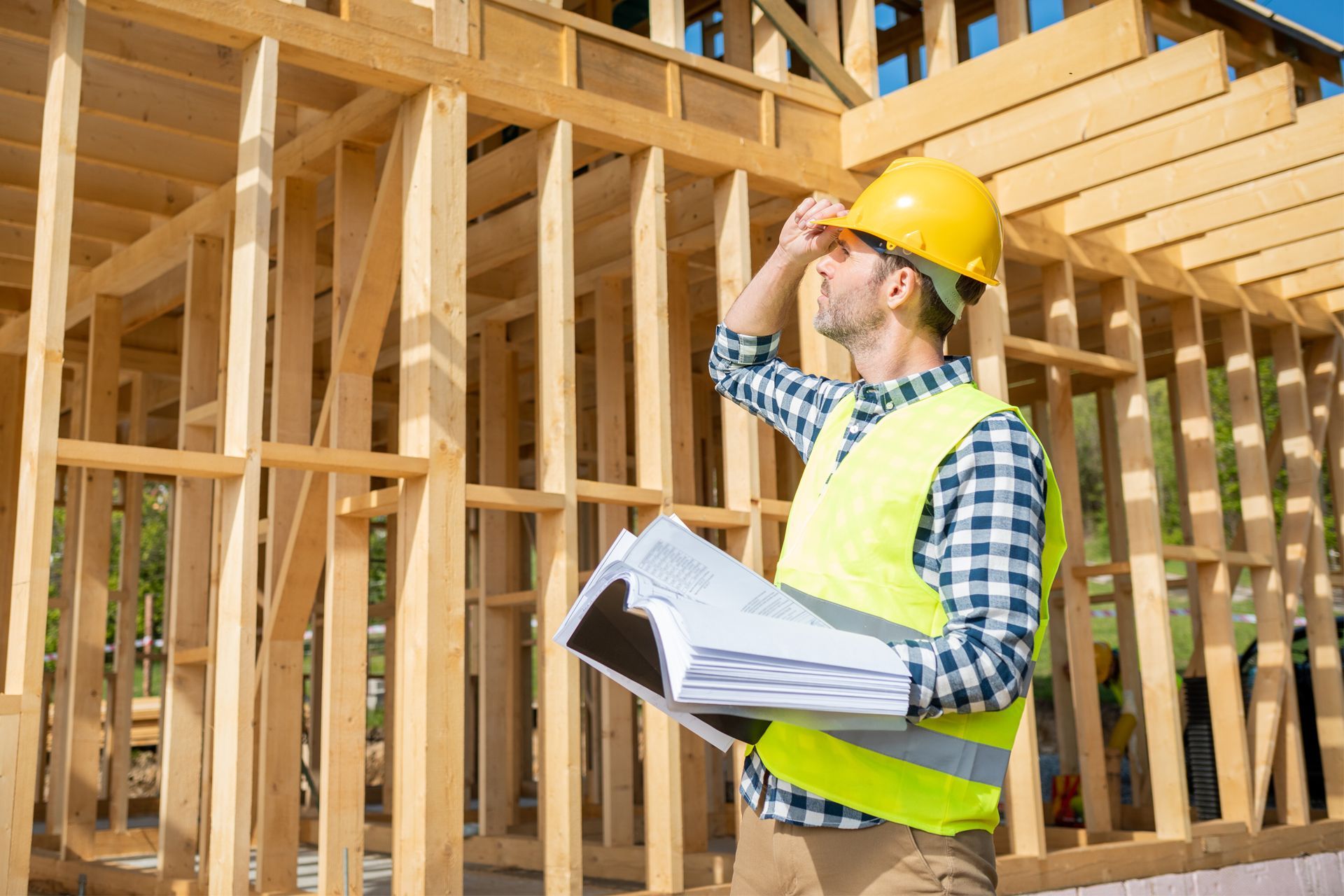 Construction worker with blueprints inspecting a wooden building frame.