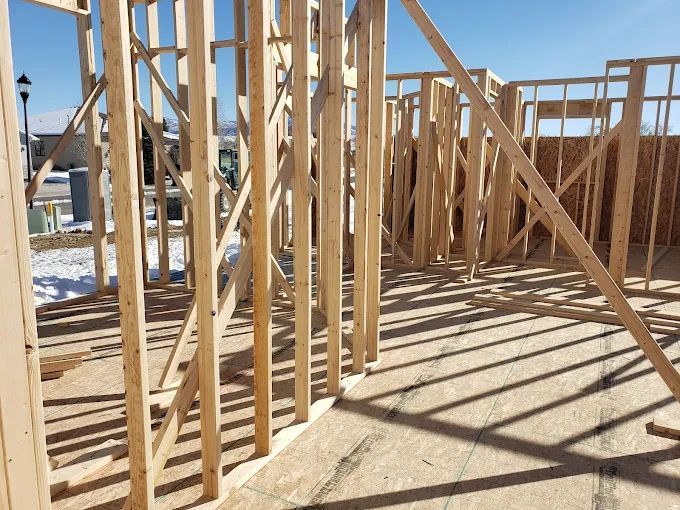Interior wooden framing of a house under construction; sunlight casts shadows on the floor.