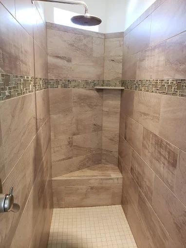Shower with light brown tiles, a small built-in bench, and a decorative mosaic tile border.