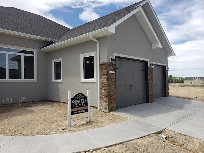 Exterior view of a two-car garage attached to a house, with a Quality Homes sign out front.