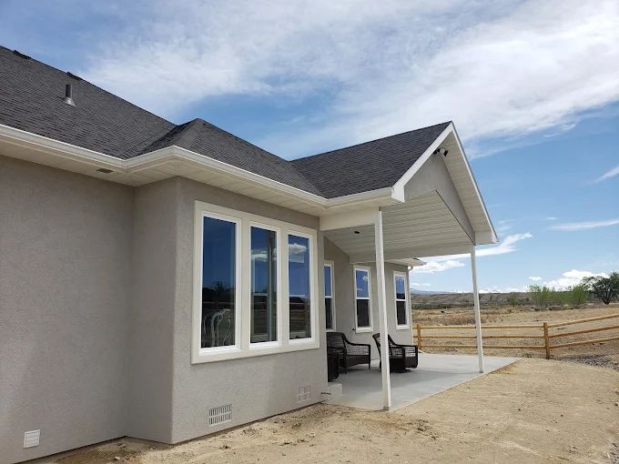 Tan stucco house with white trim, large windows, and a covered patio. Cloudy sky.