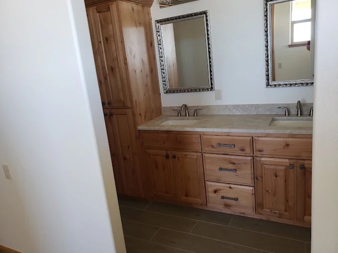 Bathroom with wooden vanity, dual sinks, mirrors, and a tall storage cabinet.