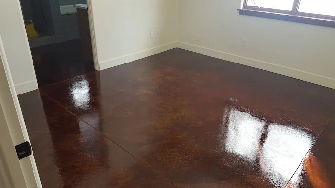 Brown, glossy stained concrete floor in an empty room with white trim and doorway.