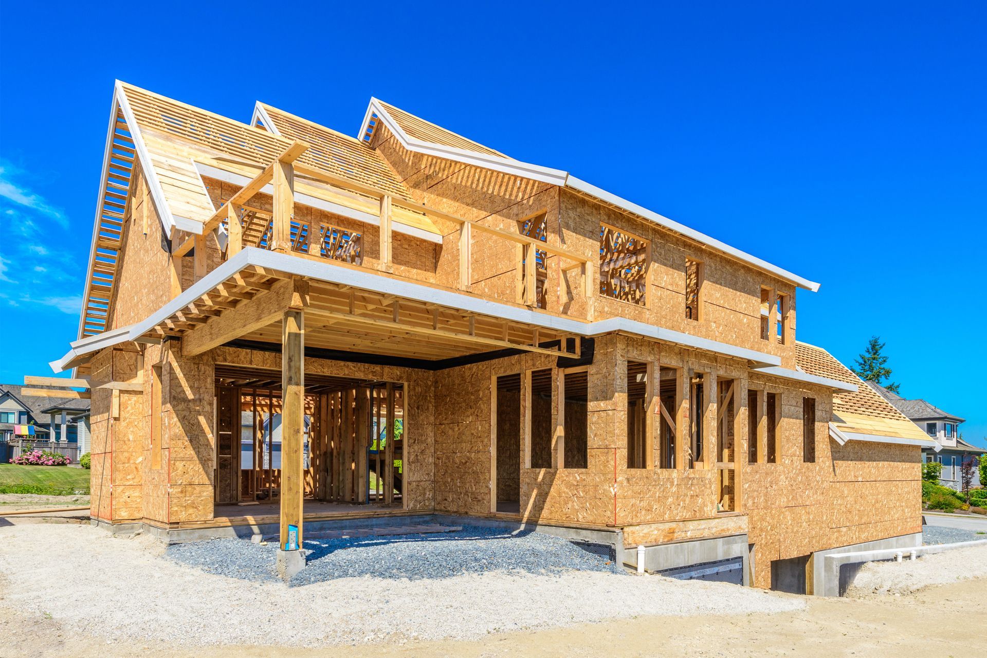 House under construction, wood framing visible, clear blue sky background.