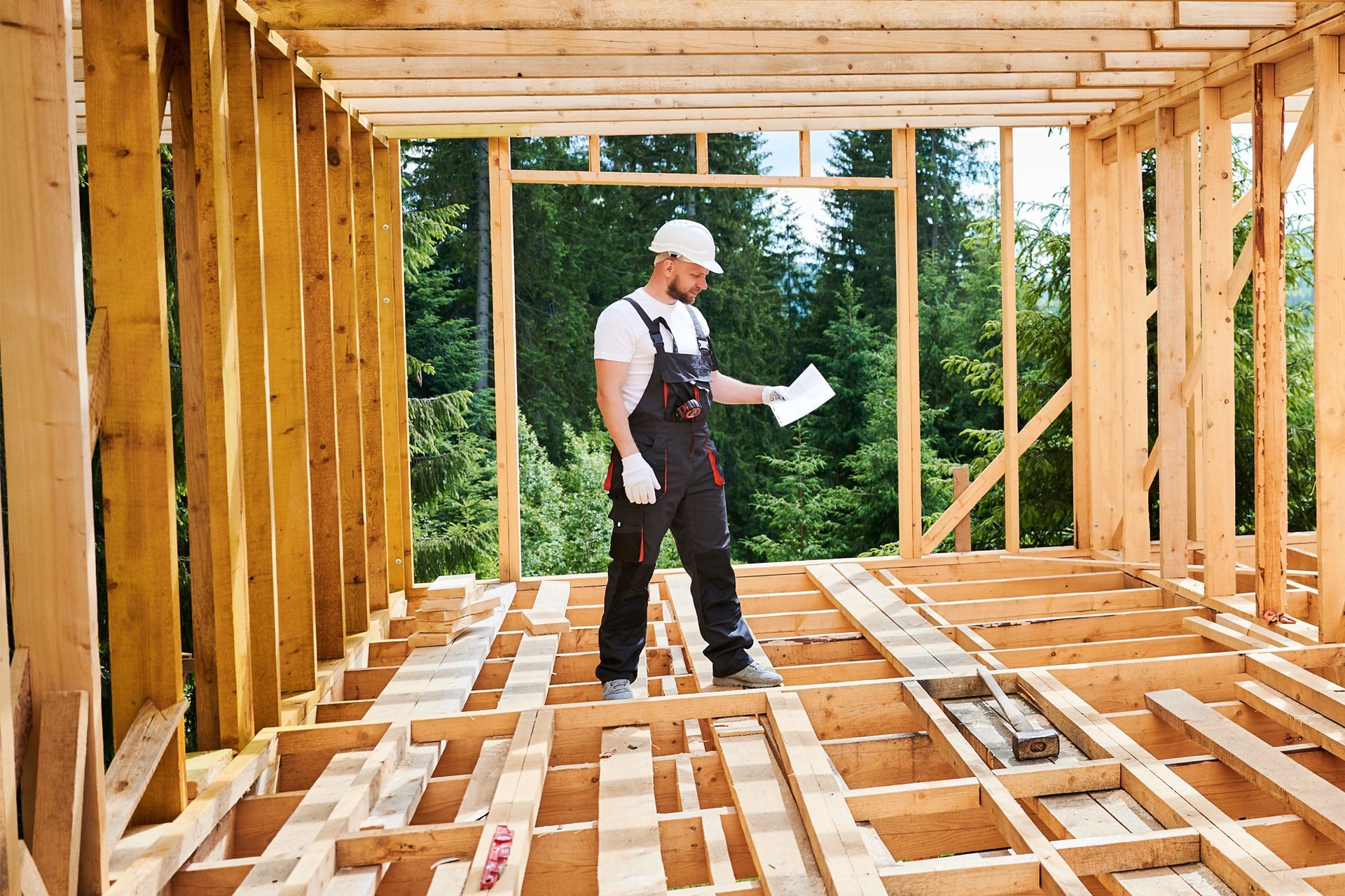 Construction worker inside unfinished wooden building, reviewing plans.
