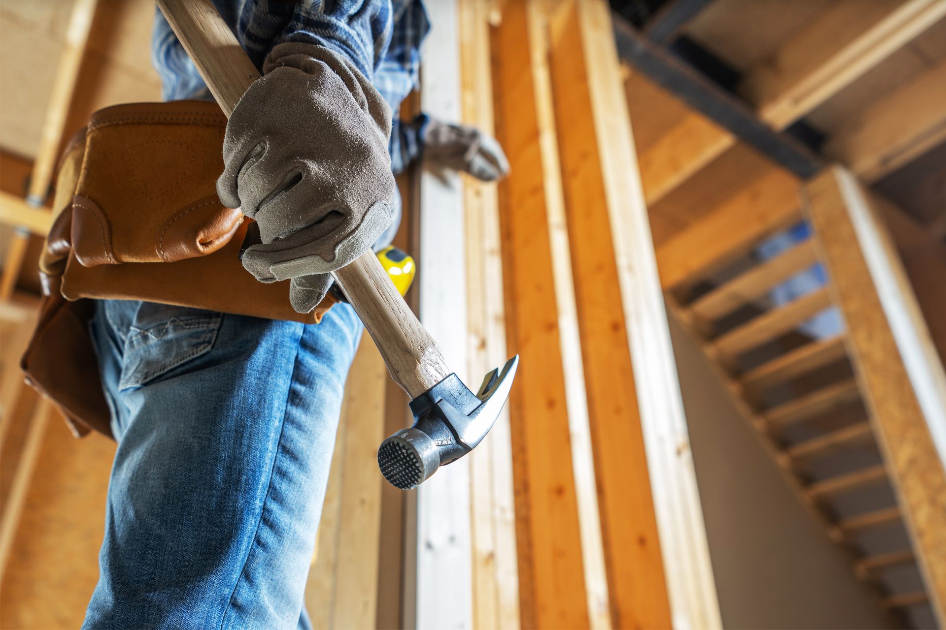 Construction worker holding hammer, wearing gloves, working on a wooden frame.