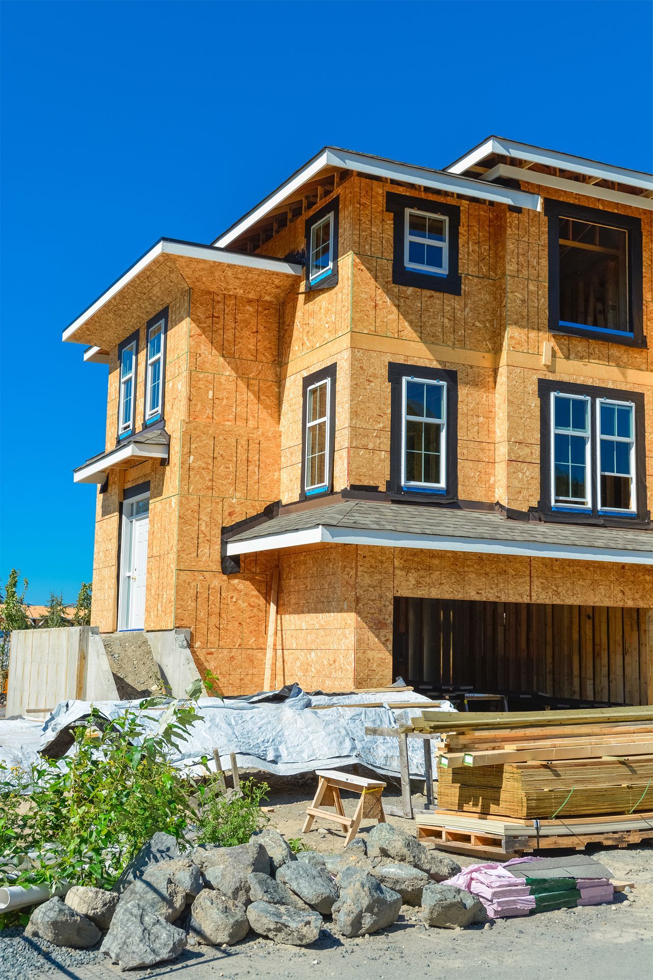 New house under construction, exposed wood frame, blue sky, building materials.
