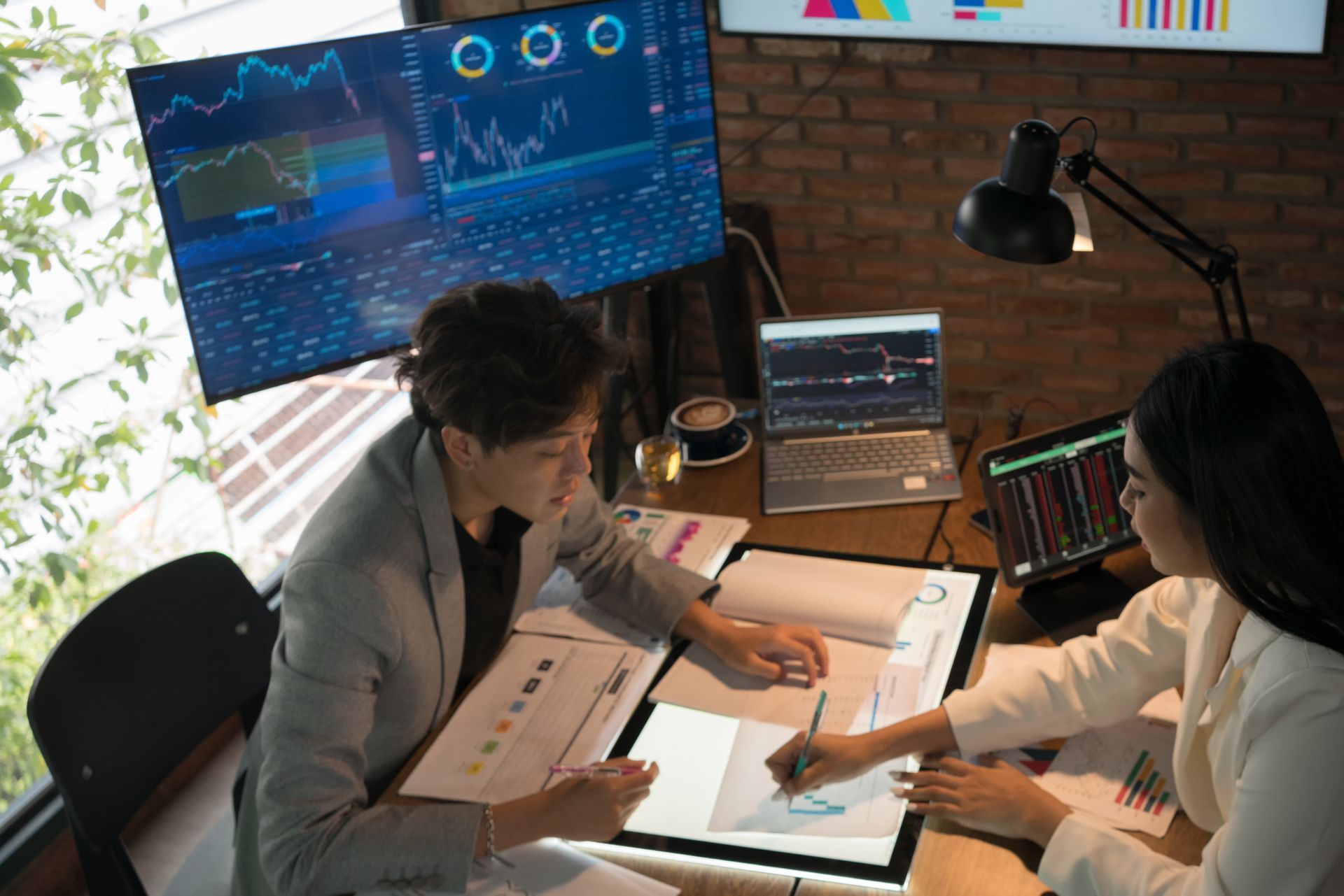 Business broker meeting with client analyzing financial charts on computer screens in office.