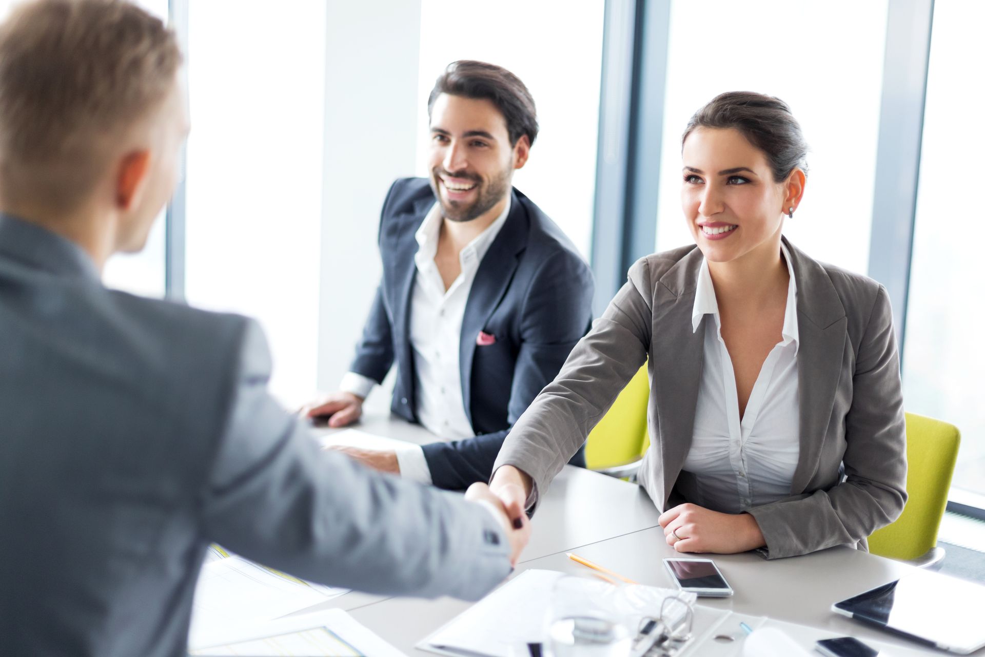 Smiling business broker firm team sealing a deal with handshake in modern office setting.