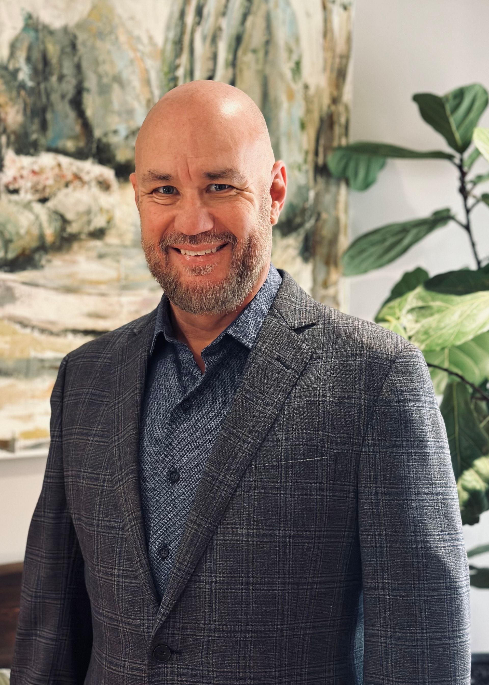 A bald man with a beard is wearing a blue sweater and smiling.