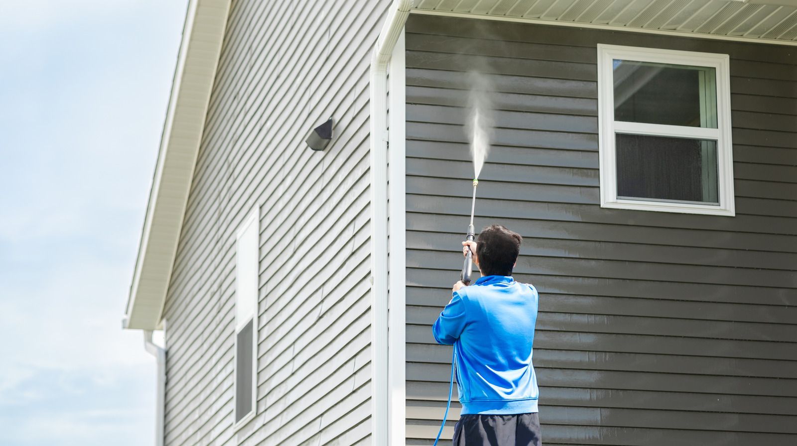 A professional cleaning service pressure washing a building facade with a high-pressure water jet.