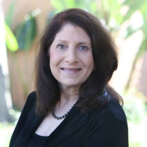 A woman wearing a black shirt and a necklace is smiling for the camera.