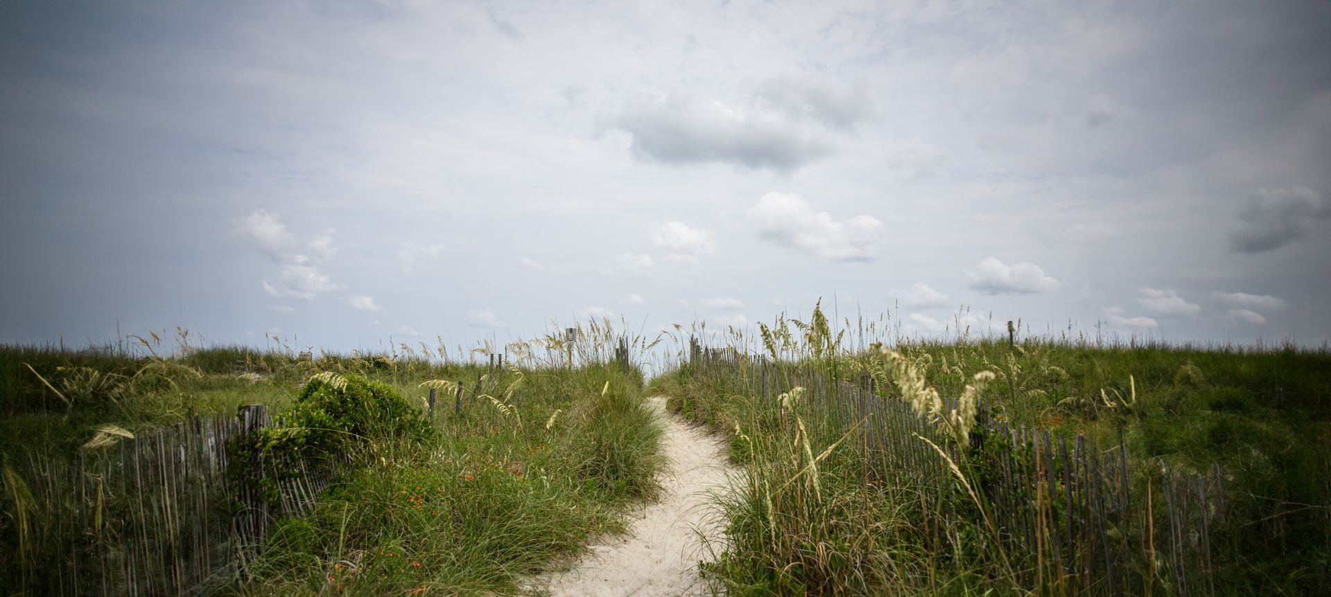 A dirt path going through a grassy field on a cloudy day.