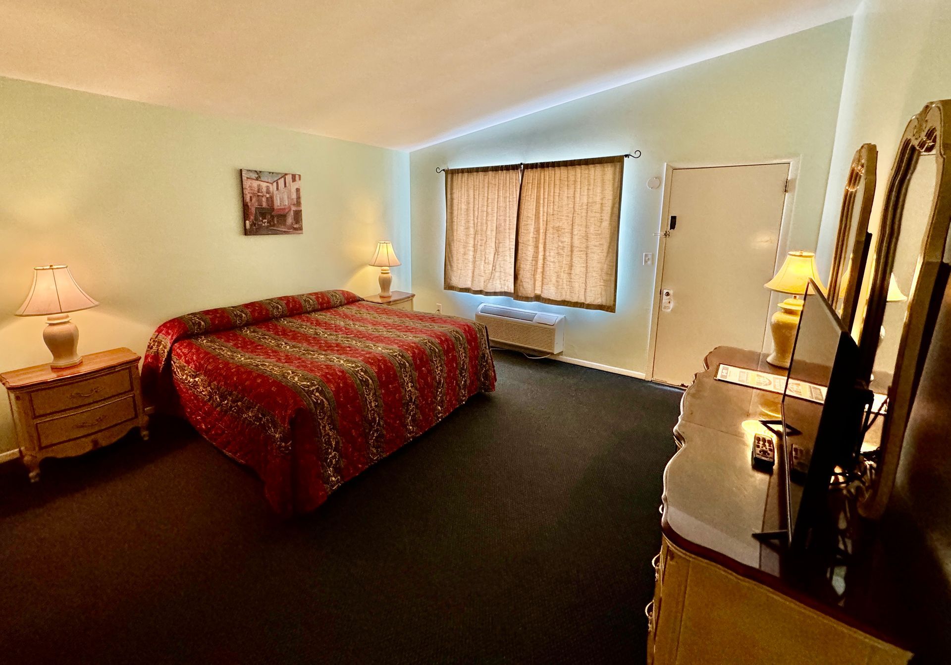A hotel room with a king size bed and a dresser.
