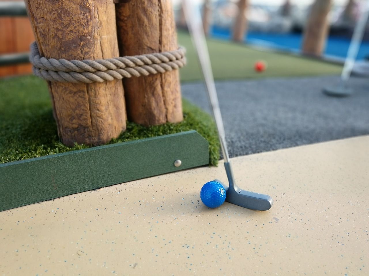 A blue golf ball is on the ground next to a golf club.
