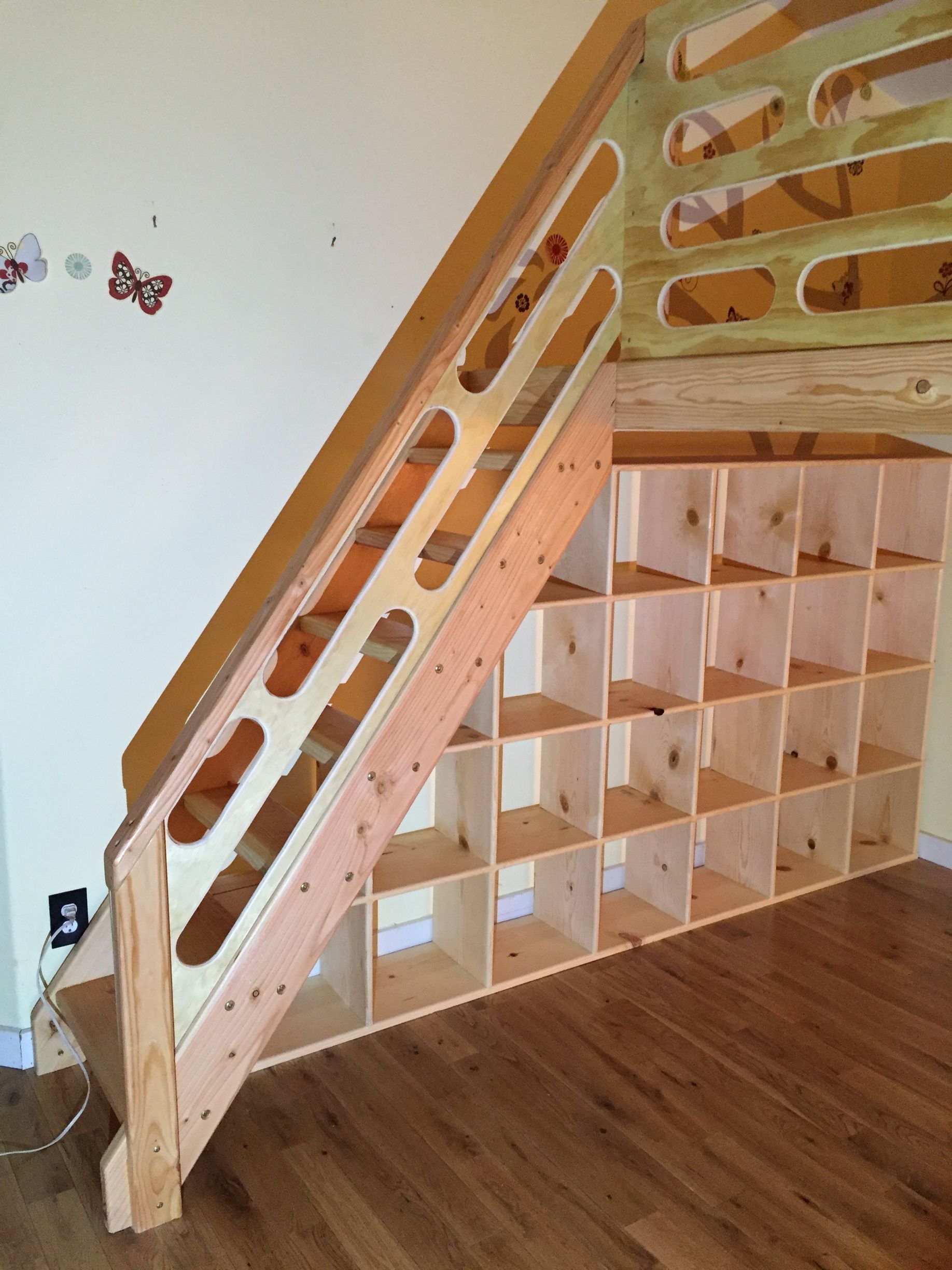 Light-colored wooden staircase built over a grid of open cubby storage shelves in a room with wood flooring.