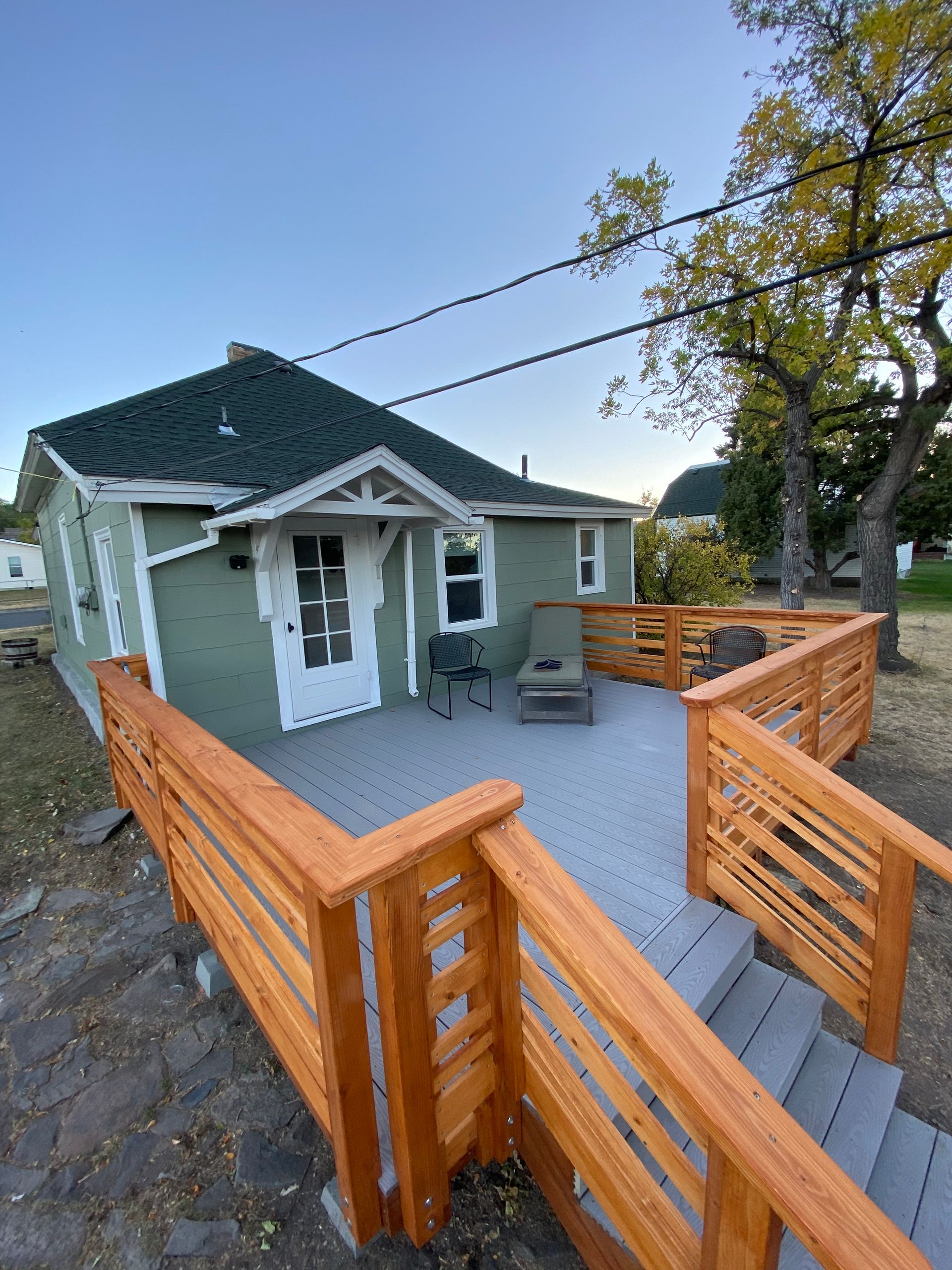 A sage green house with a white front door and a newly built wood deck with grey composite flooring and stairs.