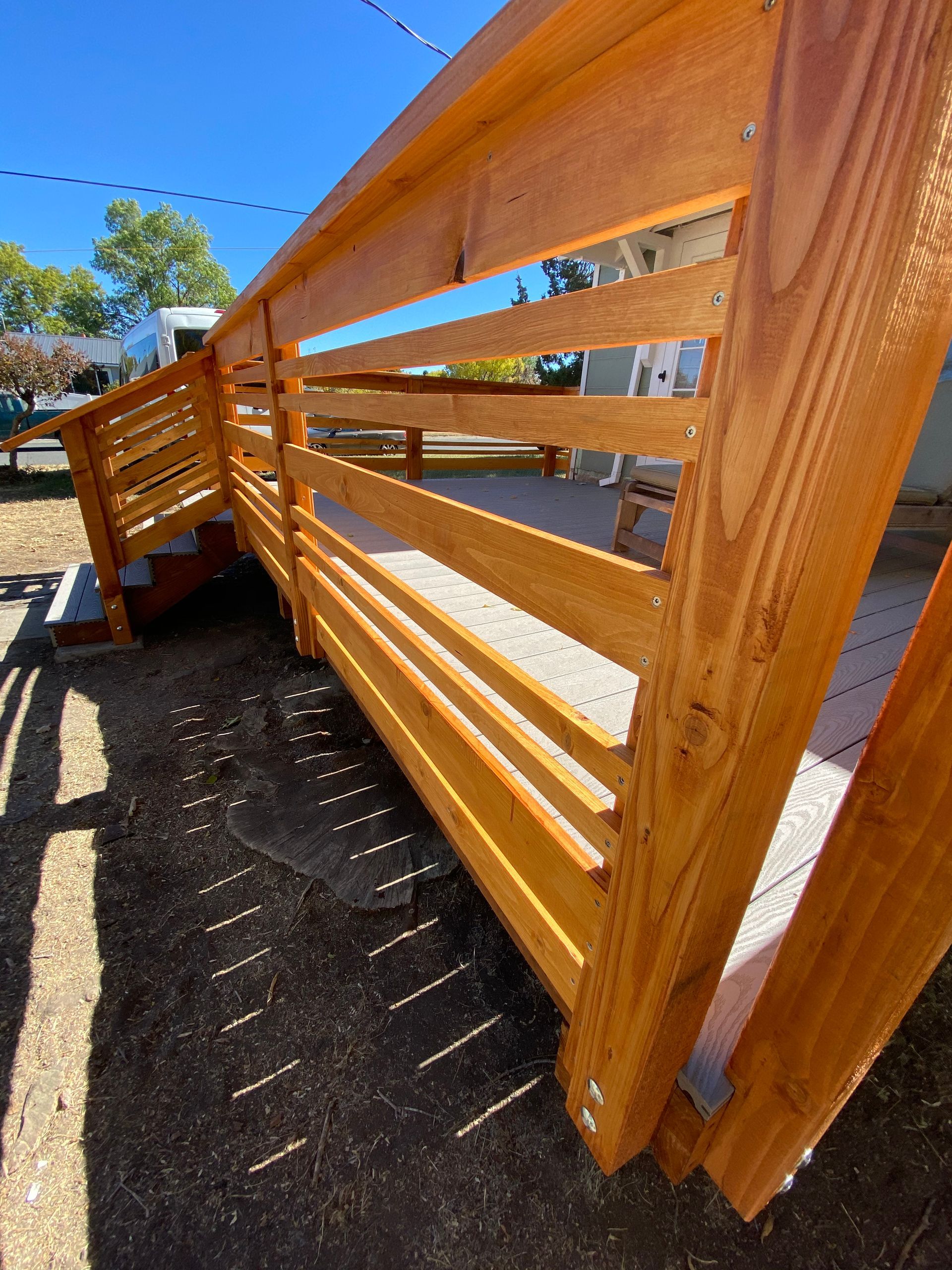 A newly constructed wooden ramp and deck railing with horizontal slats, viewed from an angle outdoors on a sunny day.