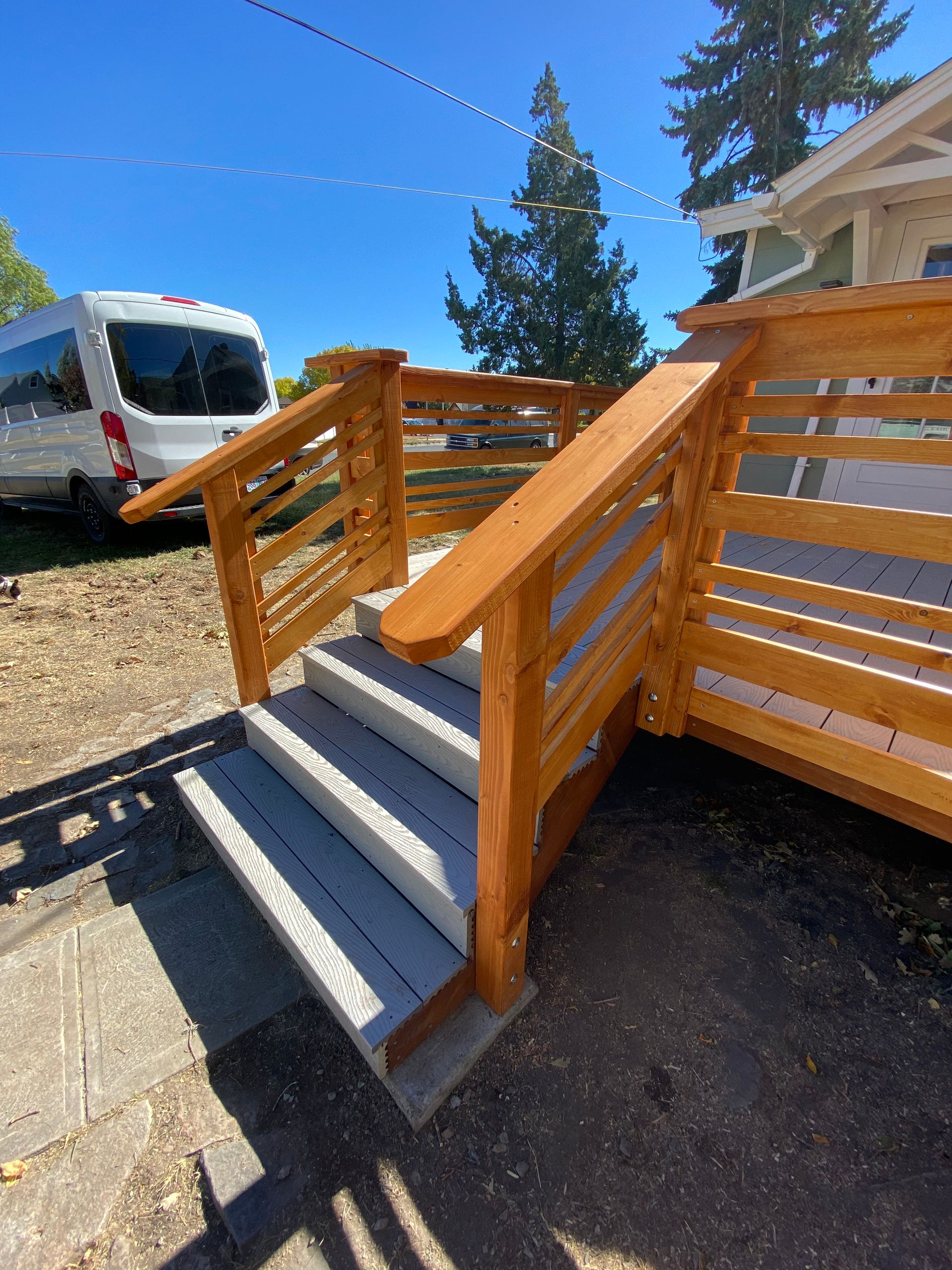 Newly built wooden staircase with a railing and gray treads, leading up to a house porch.