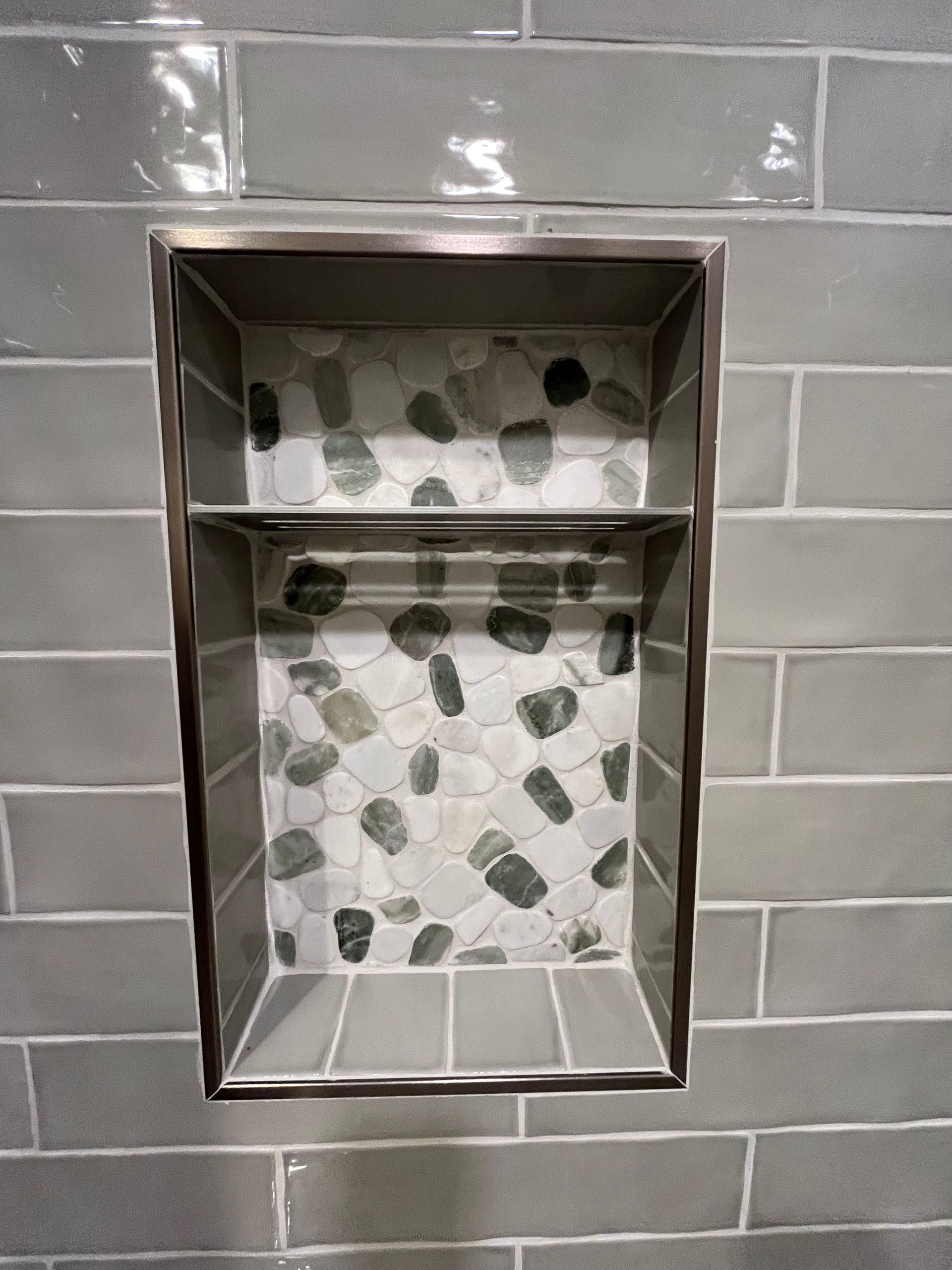 A recessed shower niche with gray subway tile walls and a decorative pebble tile back.