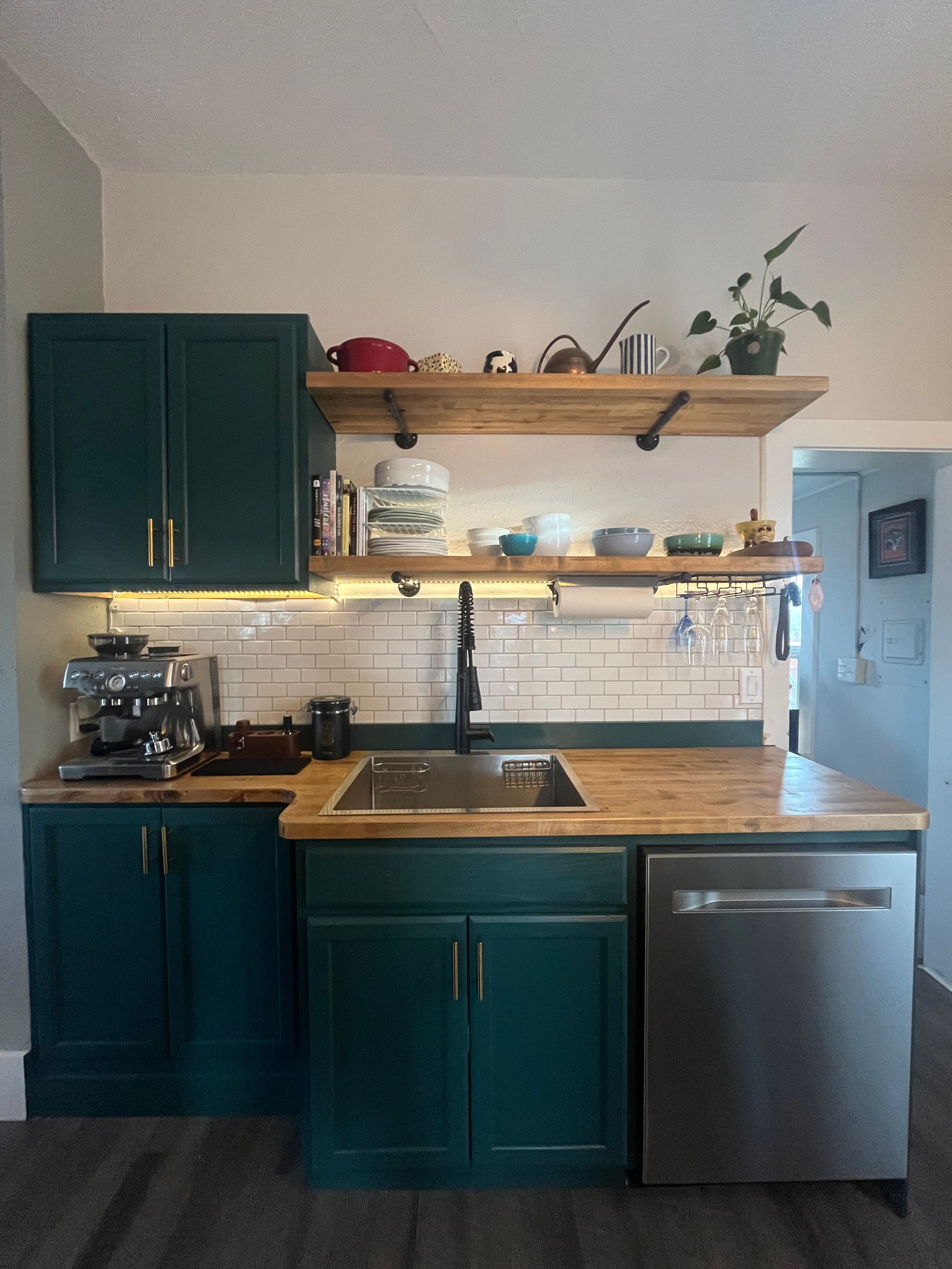 A kitchen featuring dark teal cabinets, a wooden countertop, white subway tile backsplash, and two rustic open shelves.