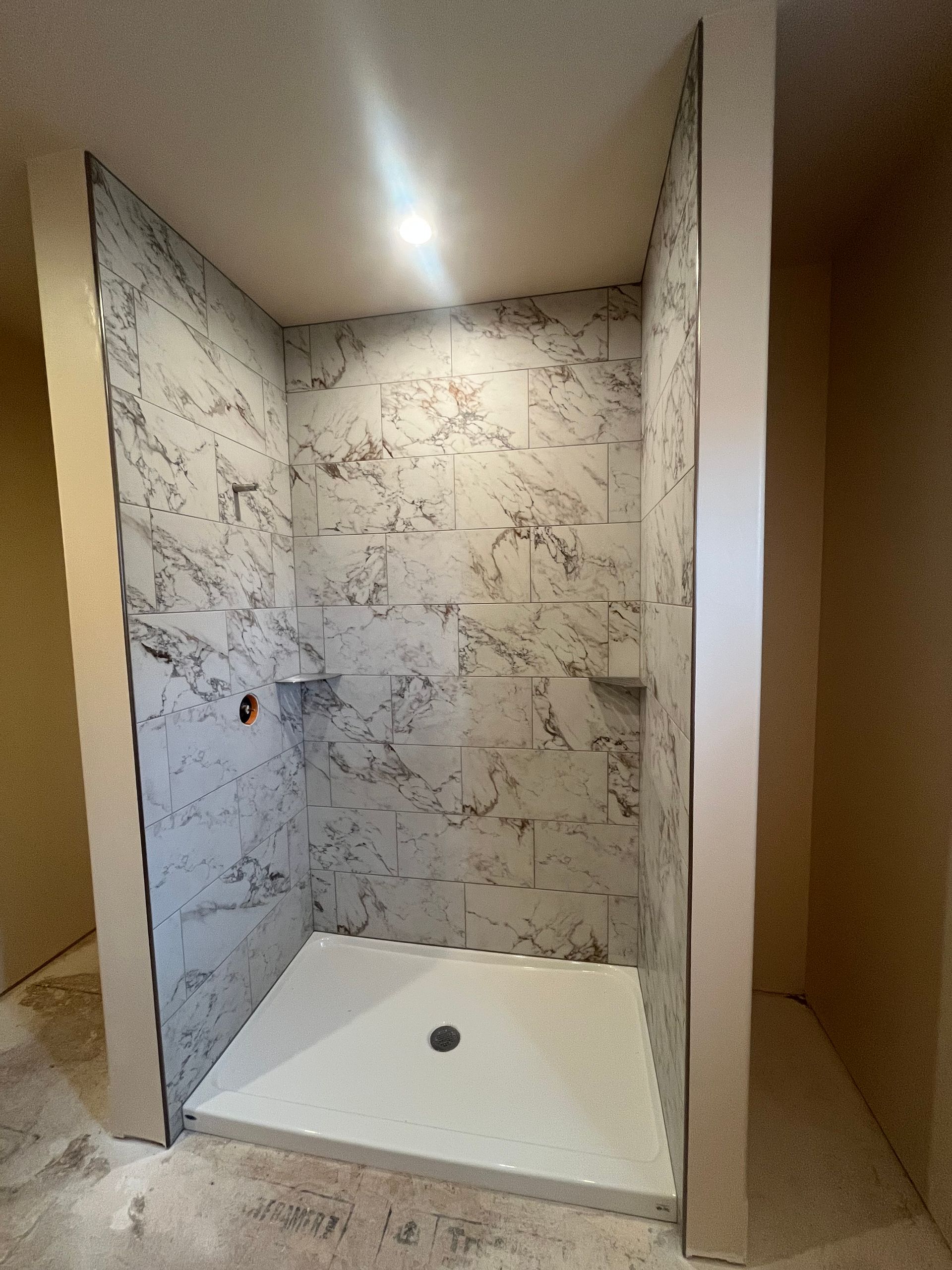 A new shower stall with white marble-patterned tile walls and a white square shower pan, currently under construction.