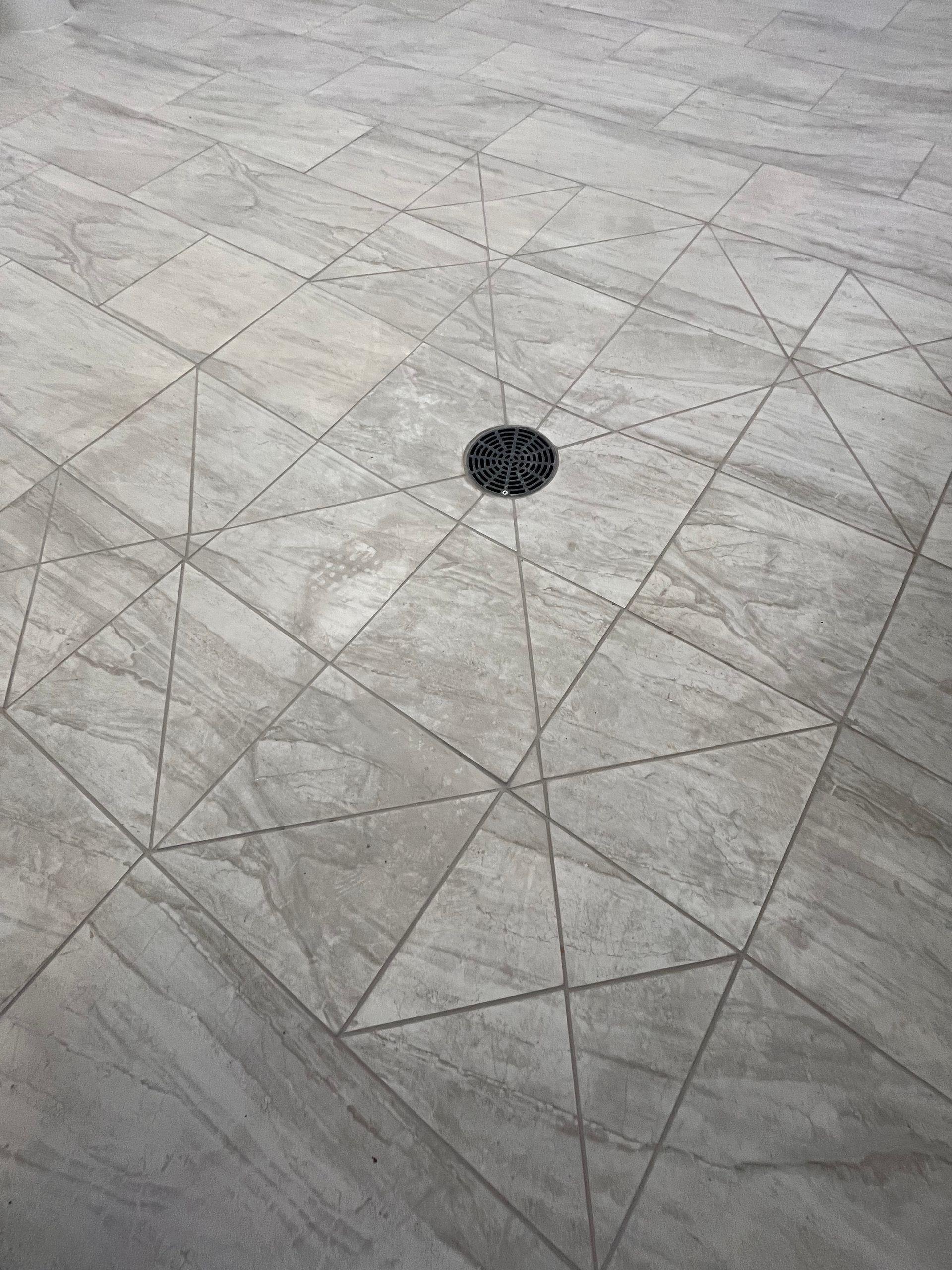 Gray stone floor tiles featuring a geometric diagonal cut pattern surrounding a central circular drain.
