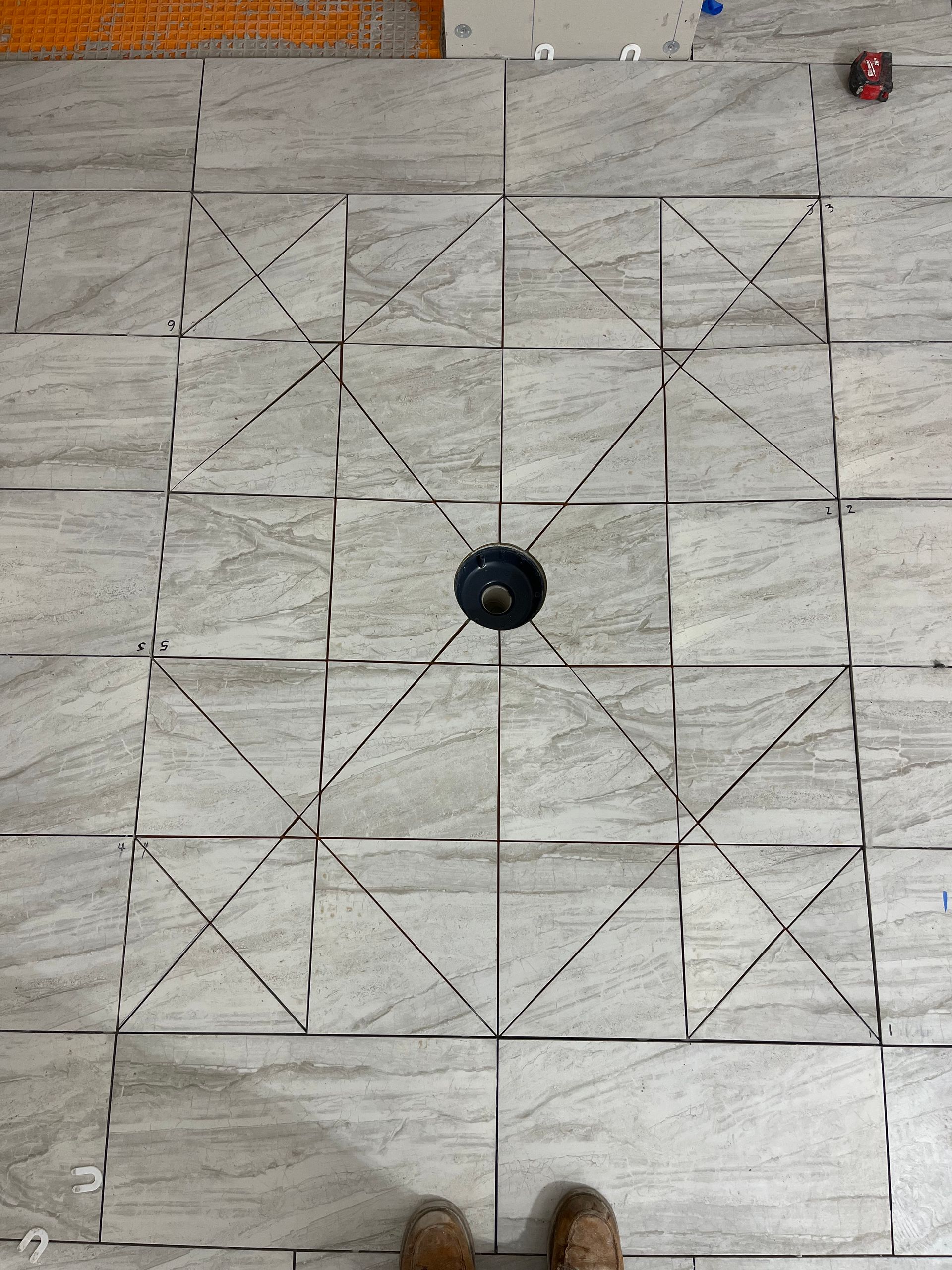 Top-down view of light-colored tile floor with pencil-drawn lines radiating from a central floor drain to create a slope.