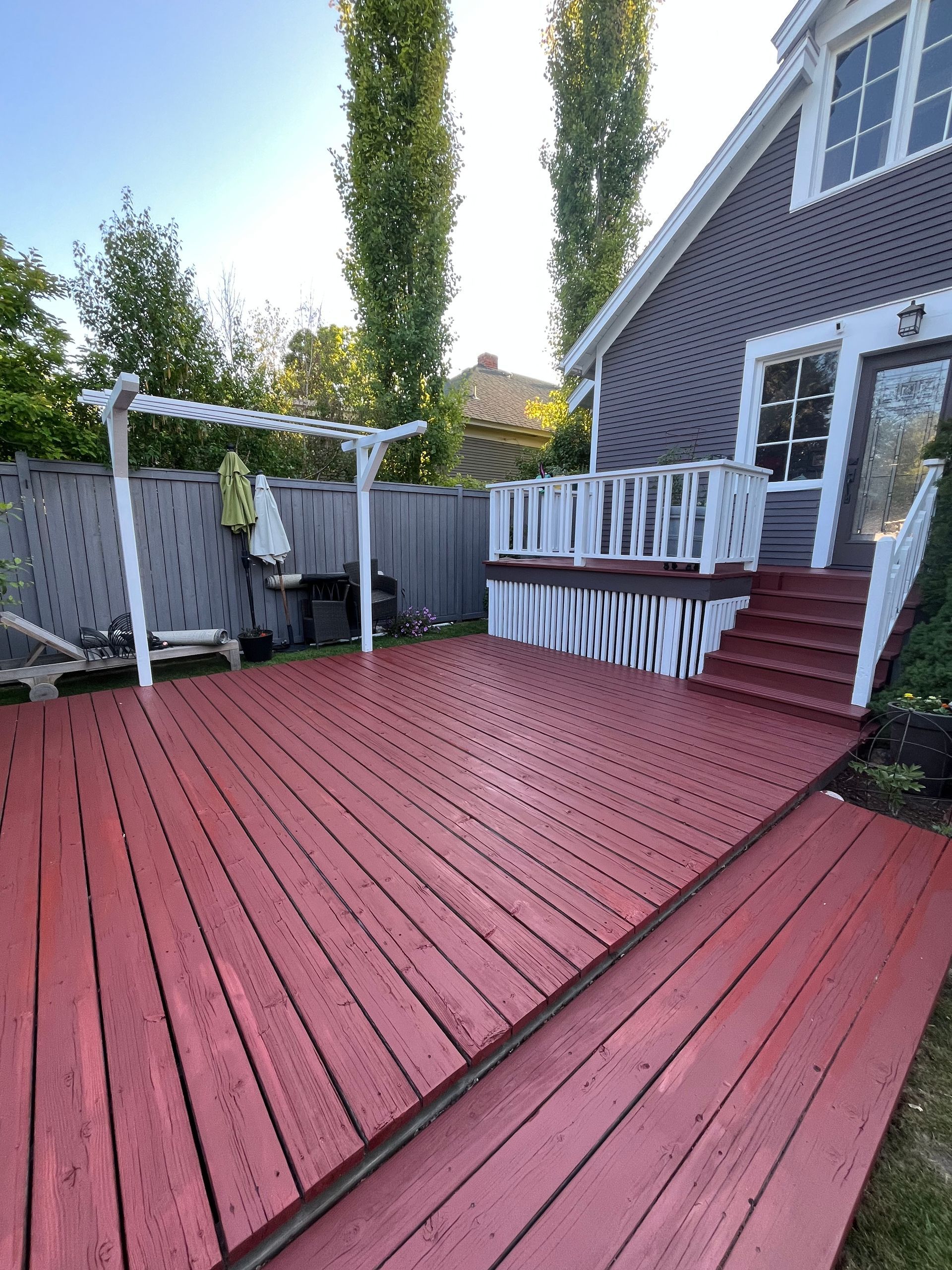 A wide-angle shot of a backyard with a large, red-stained wooden deck, white railings, and a white trellis.
