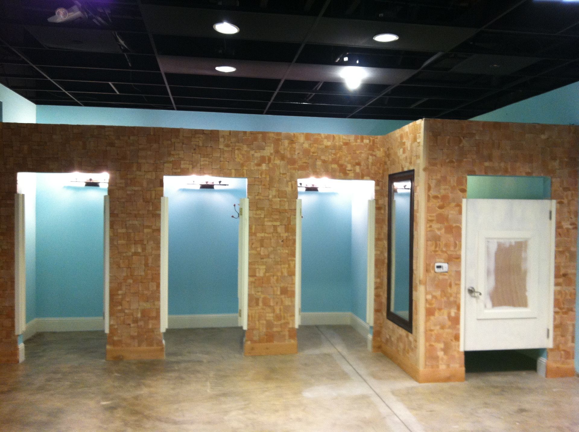 Three open dressing stalls and one closed stall with a door, set in a room with light blue walls and wood paneling.
