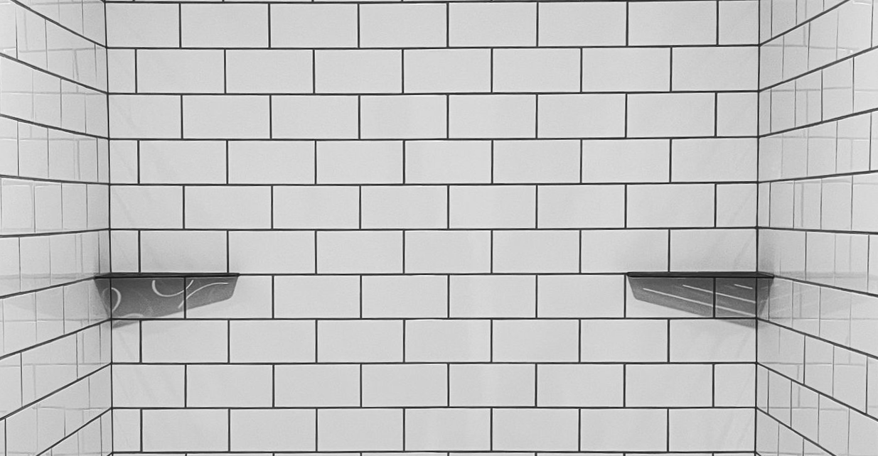 A tiled shower wall featuring white rectangular subway tiles arranged in a brick pattern with two integrated shelves.