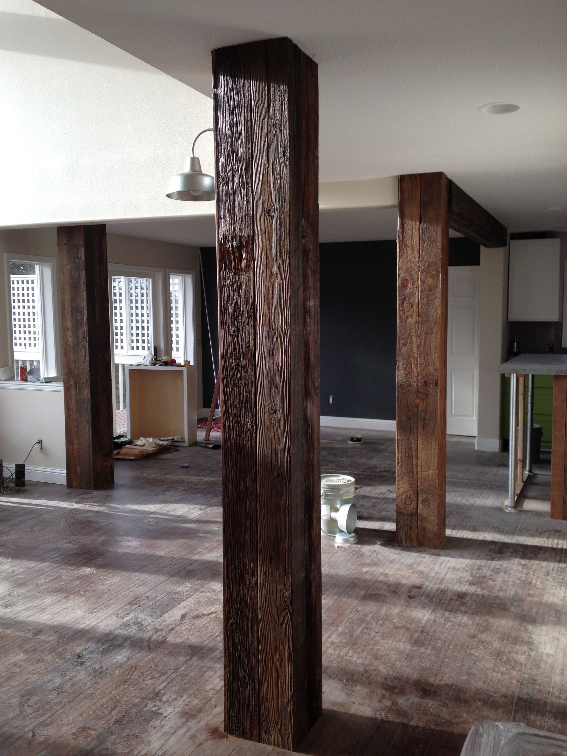 Three dark, rough-hewn wooden columns stand in an open, unfinished room with light-colored flooring and white ceilings.
