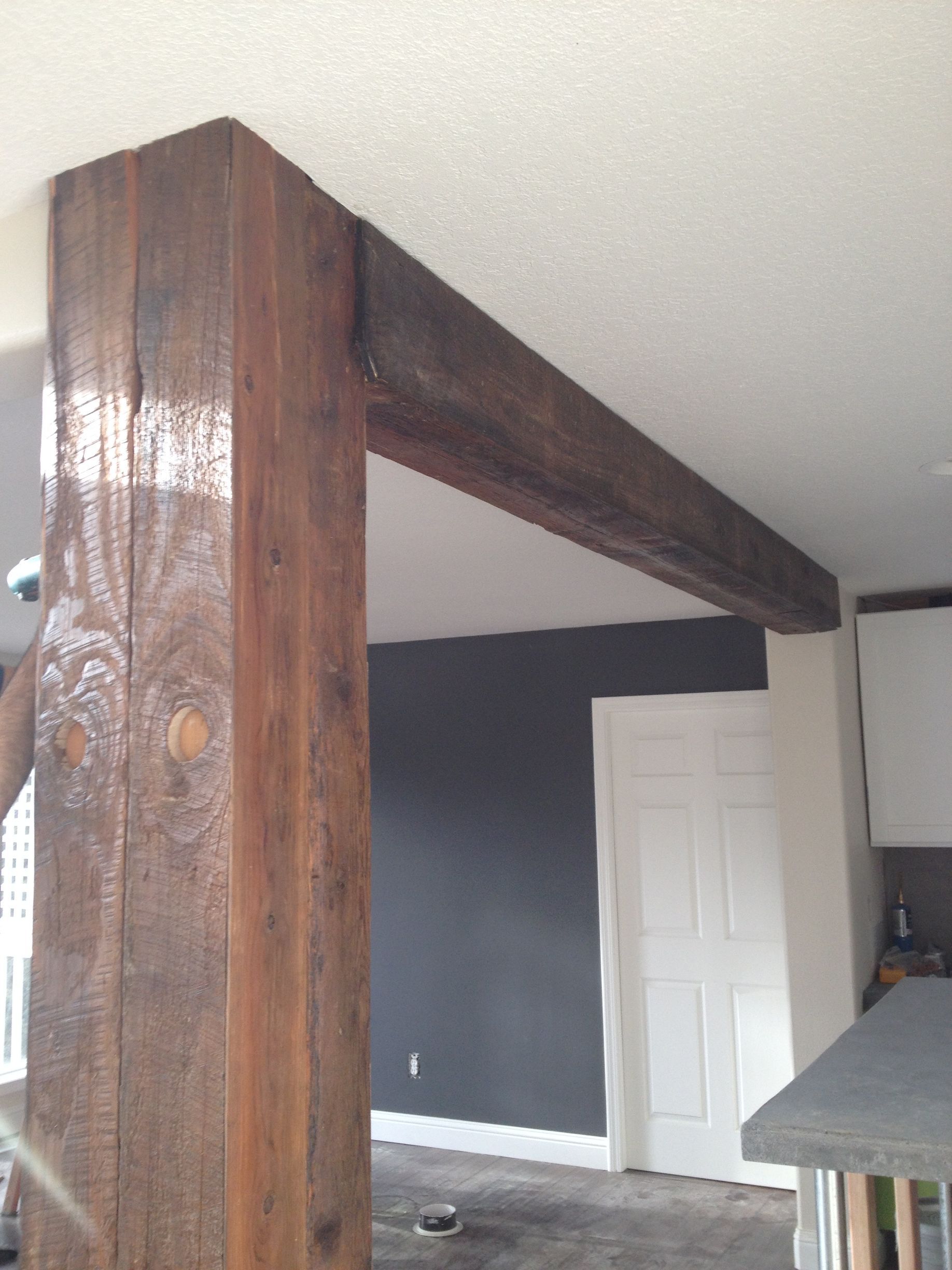 Rustic wooden beam and matching vertical support post inside a room with a white door and dark accent wall.