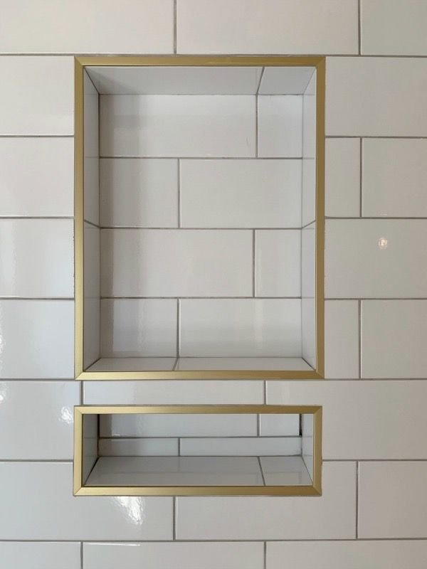Two rectangular shower niches with gold-toned metal trim set into a white subway tile wall.