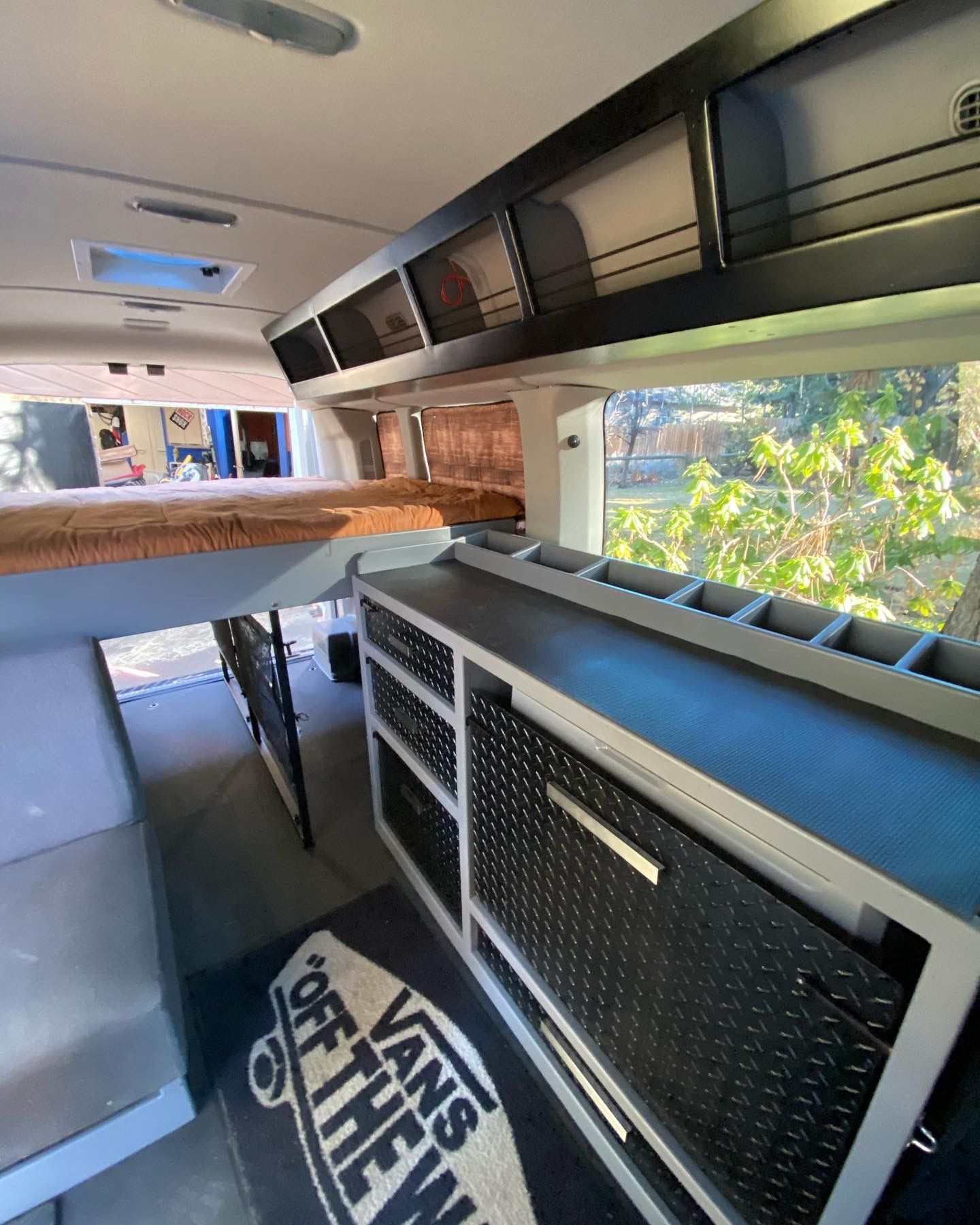 Inside a converted van showing a bed, black storage cabinets, a counter, and a 