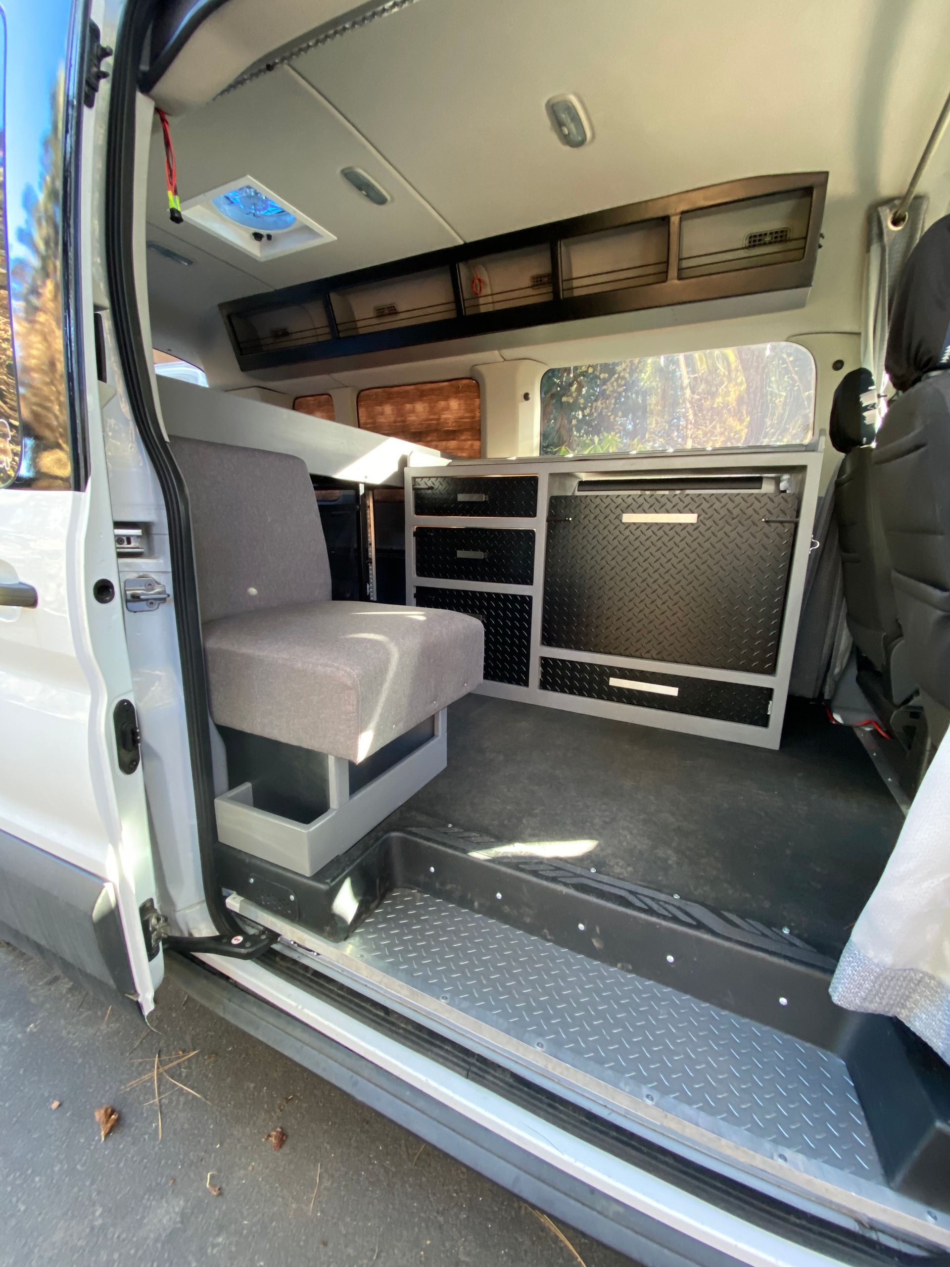 Interior of a camper van with a side seat, dark cabinets, diamond-plate trim, and a roof vent.