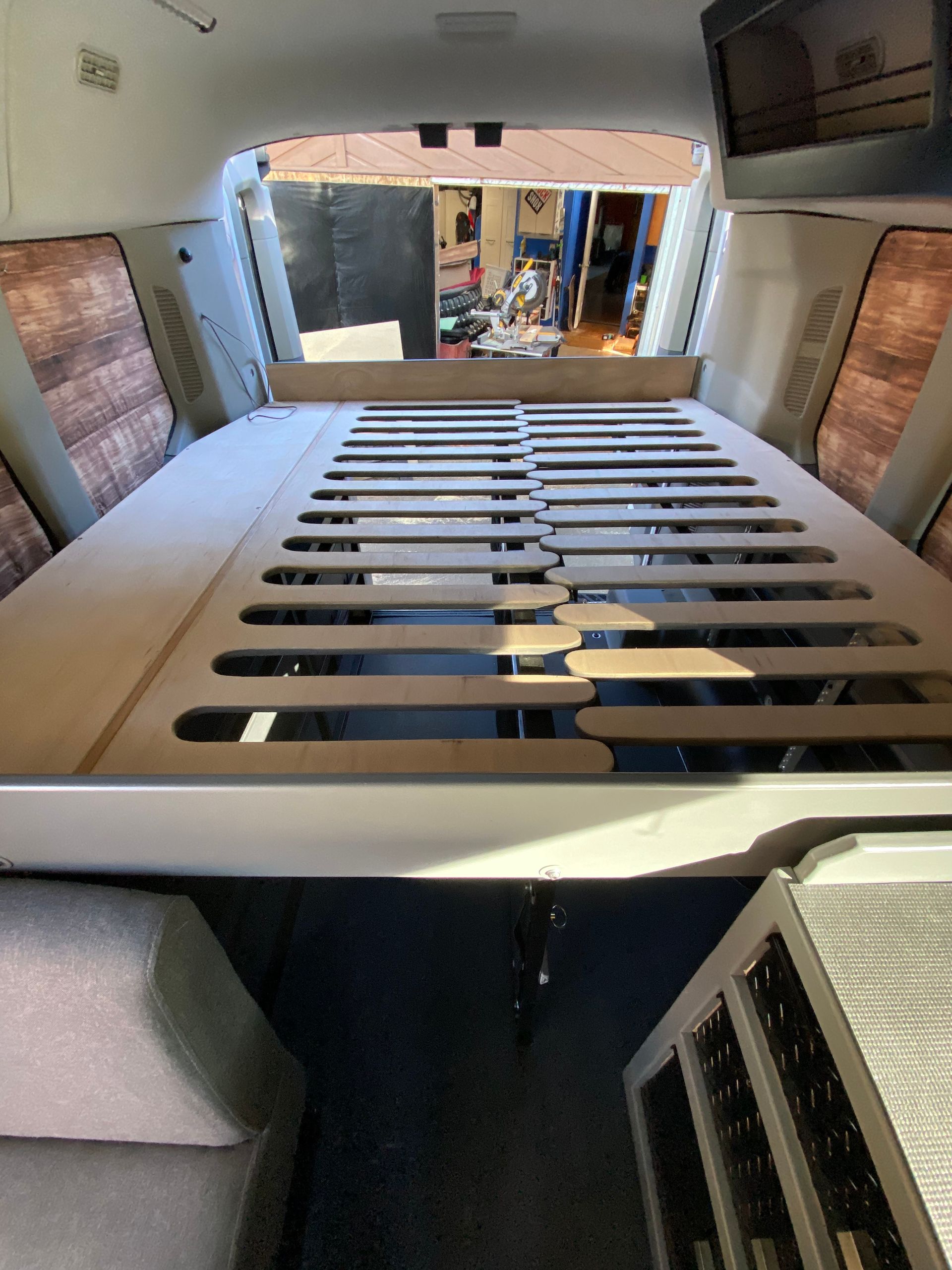 A wooden slatted bed platform inside a camper van, showing a view from the back towards the front interior.