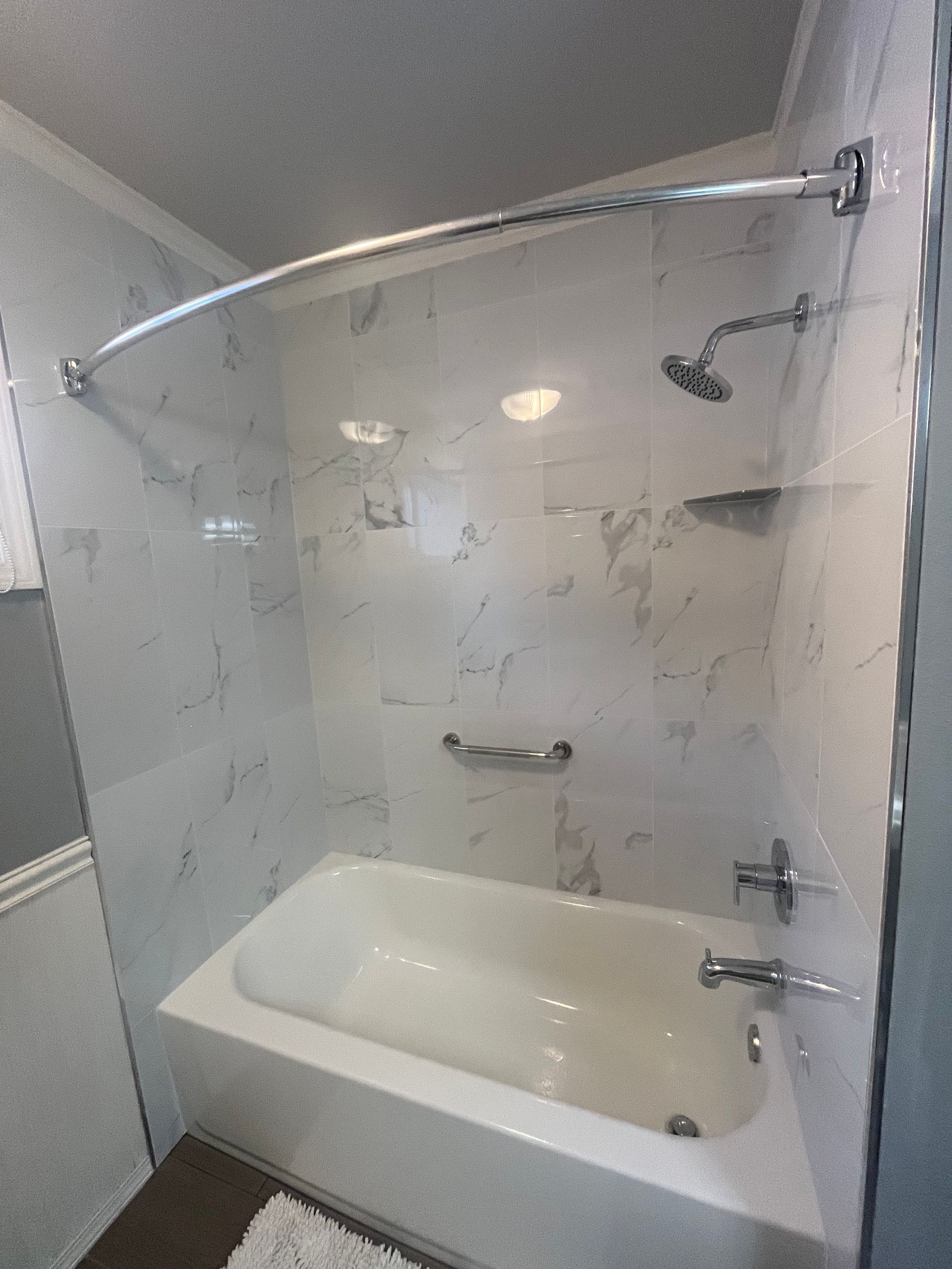 A white bathtub with marble-look tile walls, a curved shower rod, and silver fixtures in a bathroom.