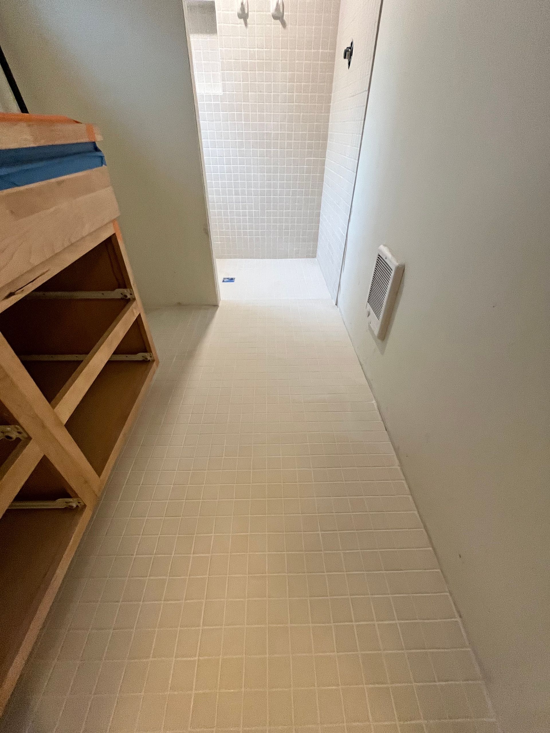 A hallway with light-colored tile flooring leading to a walk-in shower, next to unfinished wooden cabinetry.