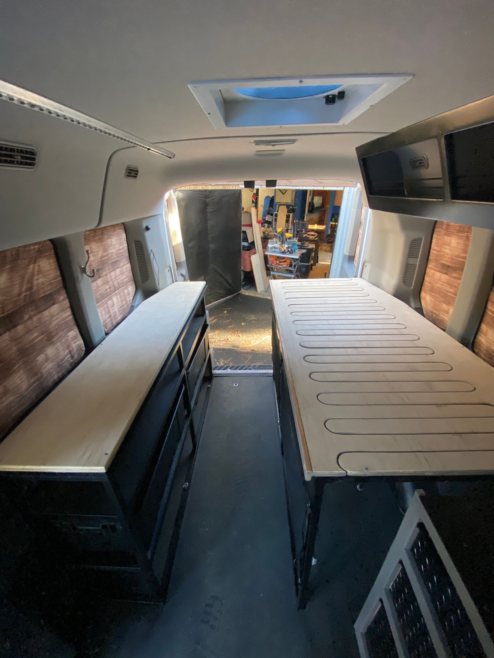 The interior of a camper van under renovation, showing two wooden platforms facing each other and a skylight above.