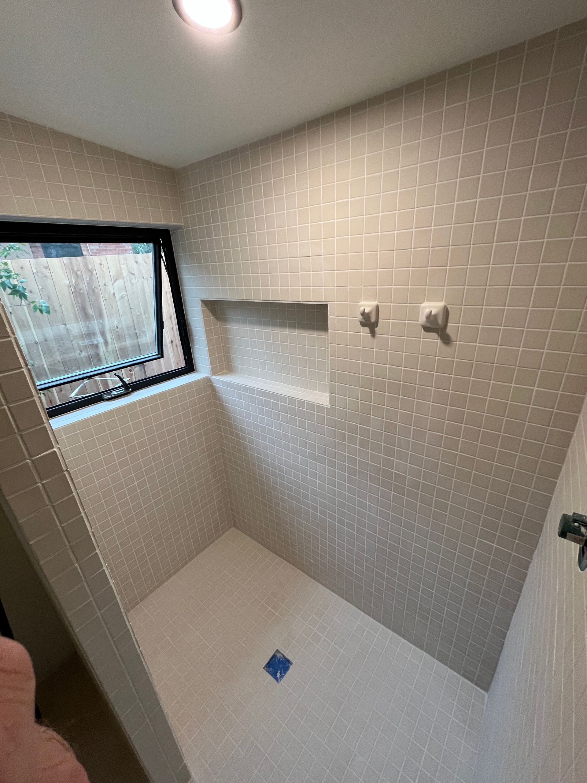 A tiled walk-in shower with a built-in recessed shelf and a window, featuring a light-colored, grid-patterned tile design.
