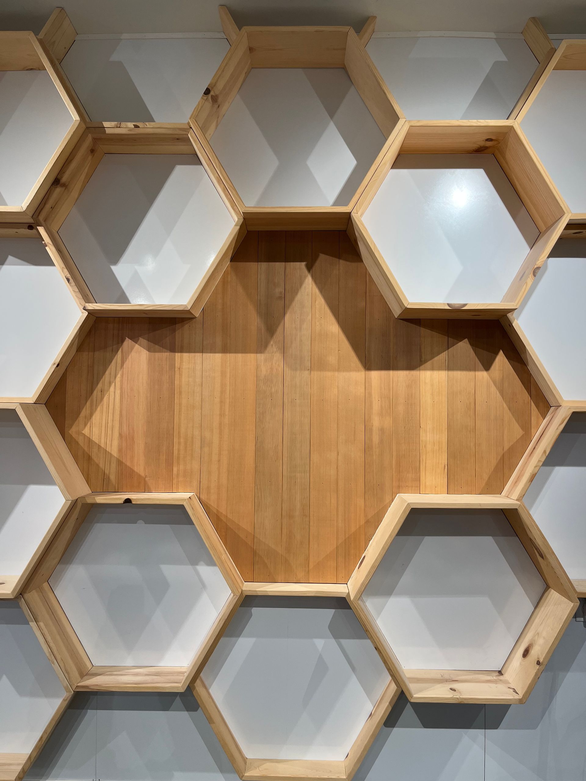 A decorative wall installation featuring modular, light wood hexagonal shelves arranged in a honeycomb pattern.