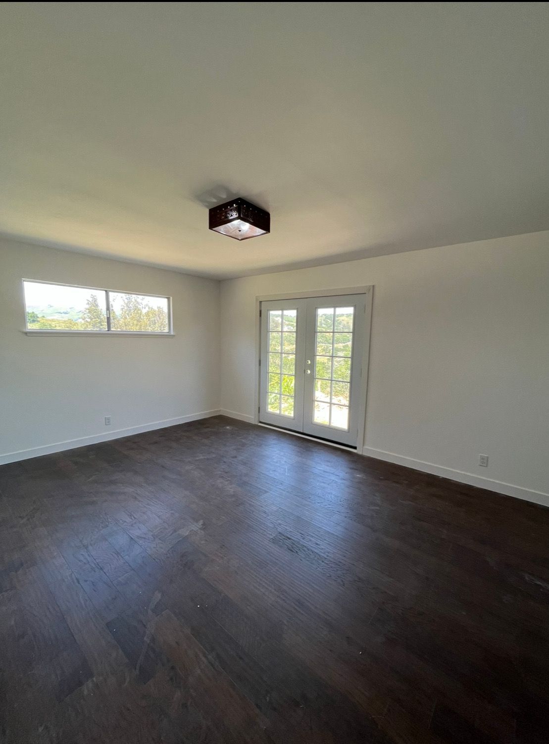 An empty room with dark herringbone wood flooring, white walls, a center flush-mount light, and glass French doors.