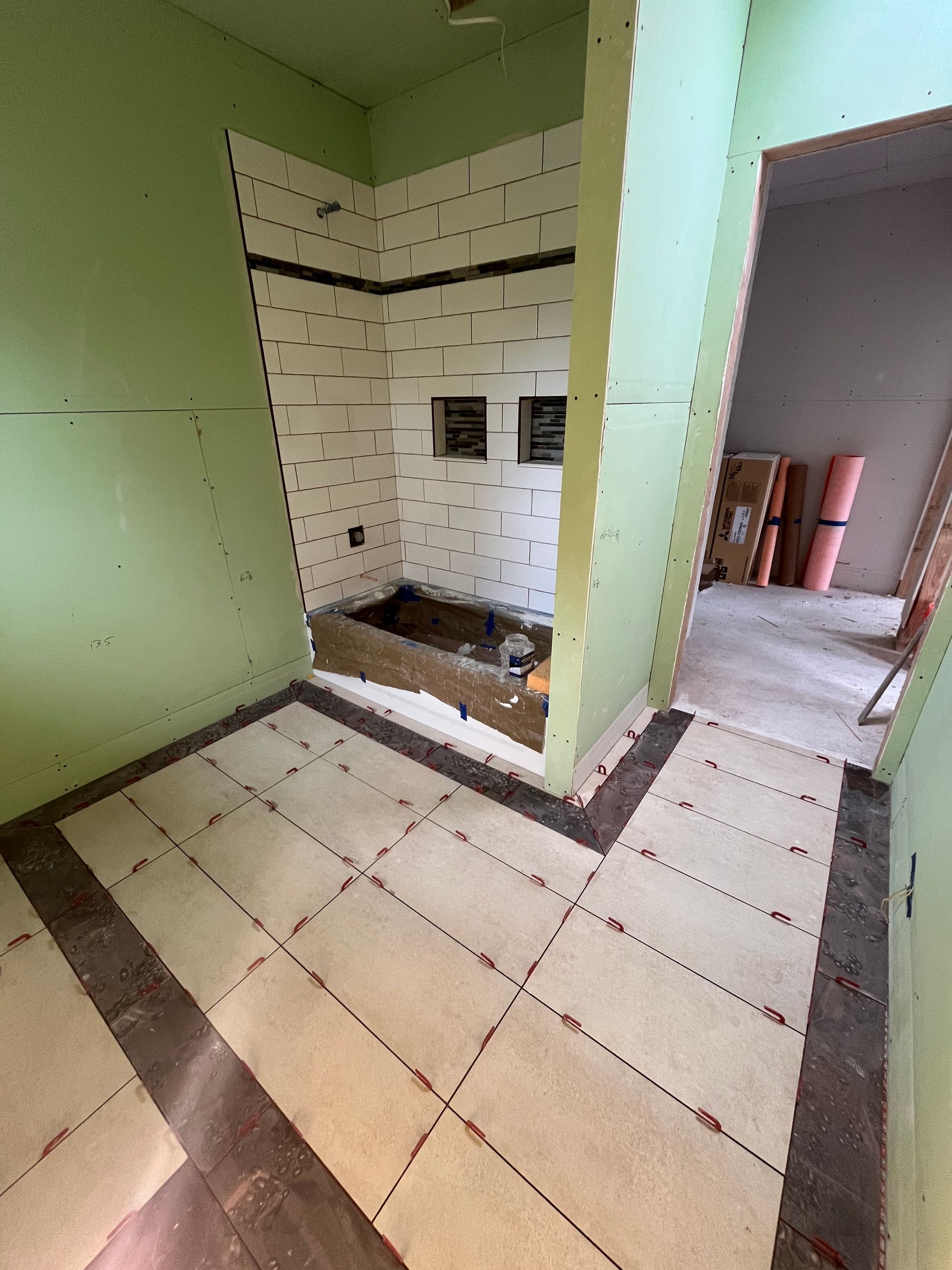 An unfinished bathroom renovation with light green walls, beige floor underlayment, and a recessed shower area.