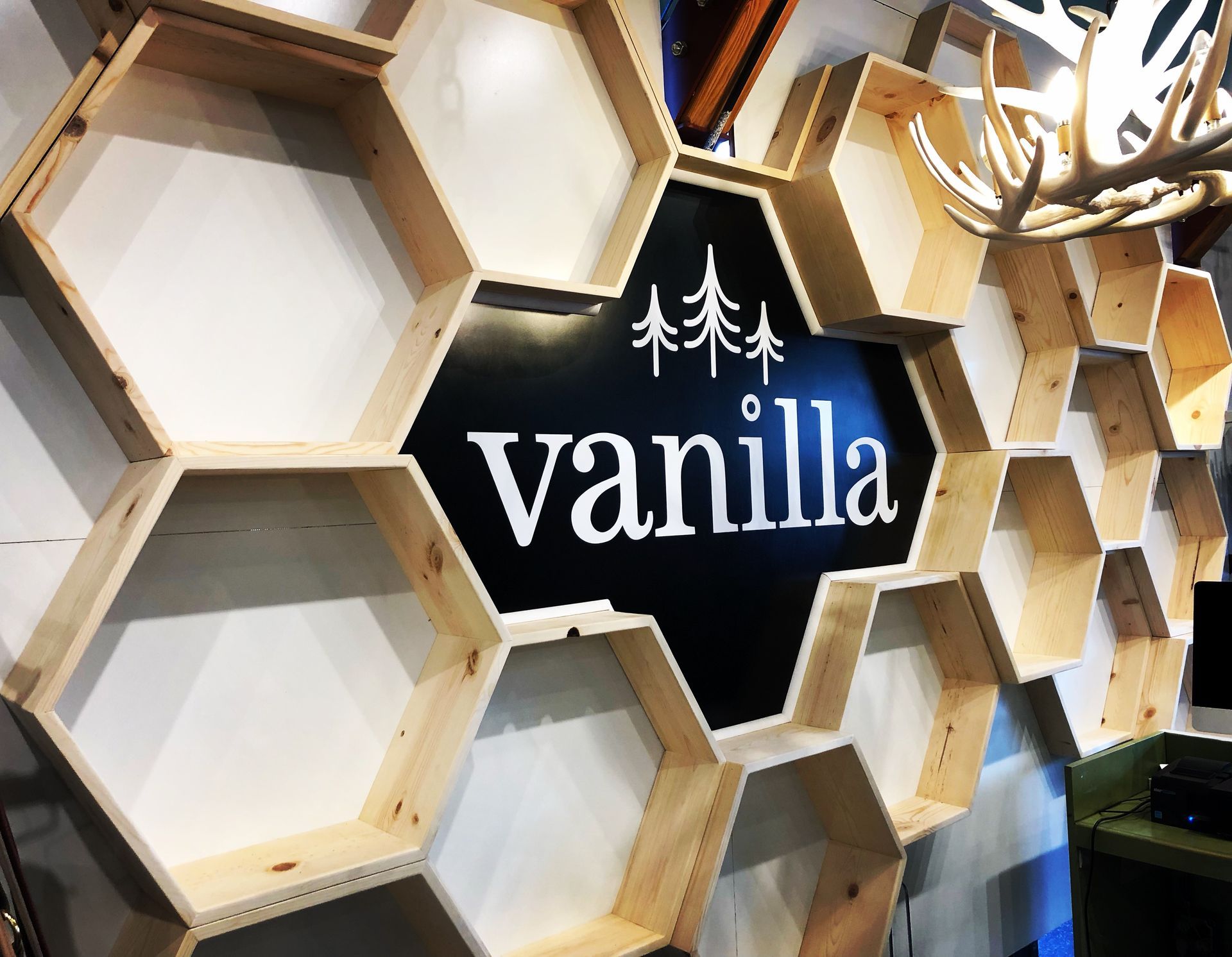 A wall display of light-wood hexagonal shelves surrounding a central black sign with white text that reads 